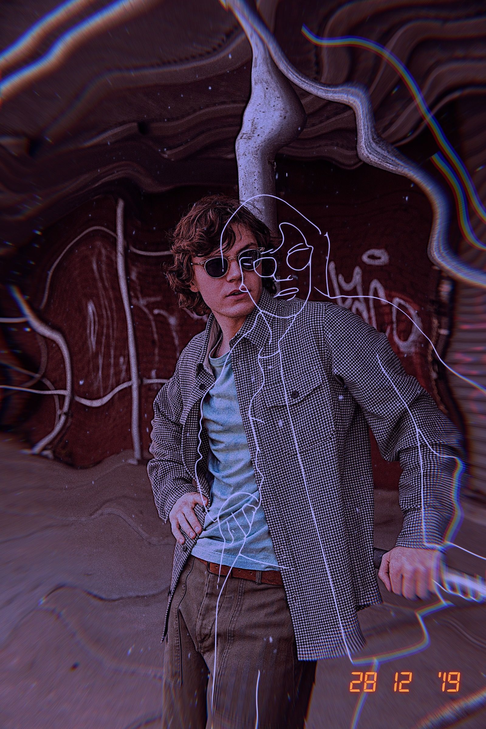 A man with sunglasses standing in front of a wall with graffiti. - Evan Peters