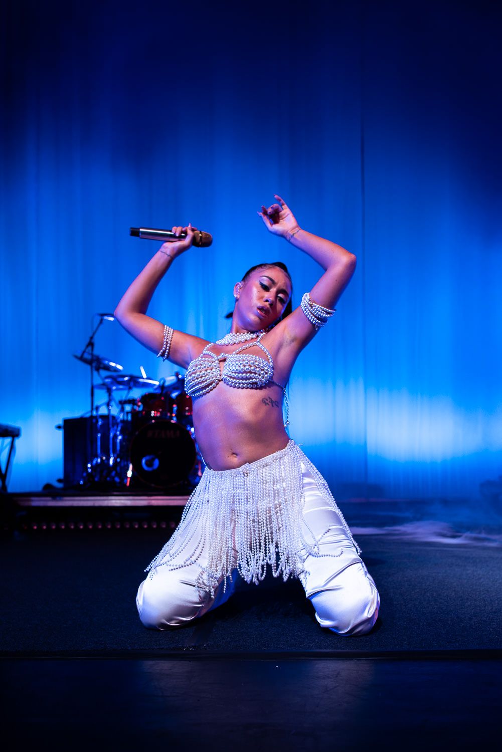 A woman wearing a white belly dance outfit is performing on stage. - Kali Uchis