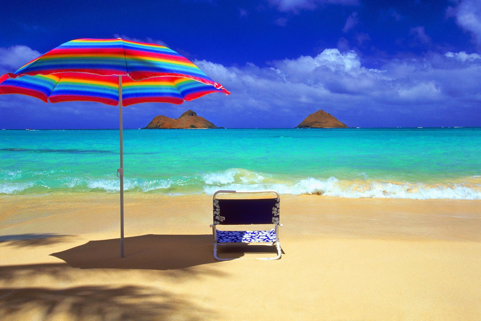 A beach chair under an umbrella on the sand - Hawaii