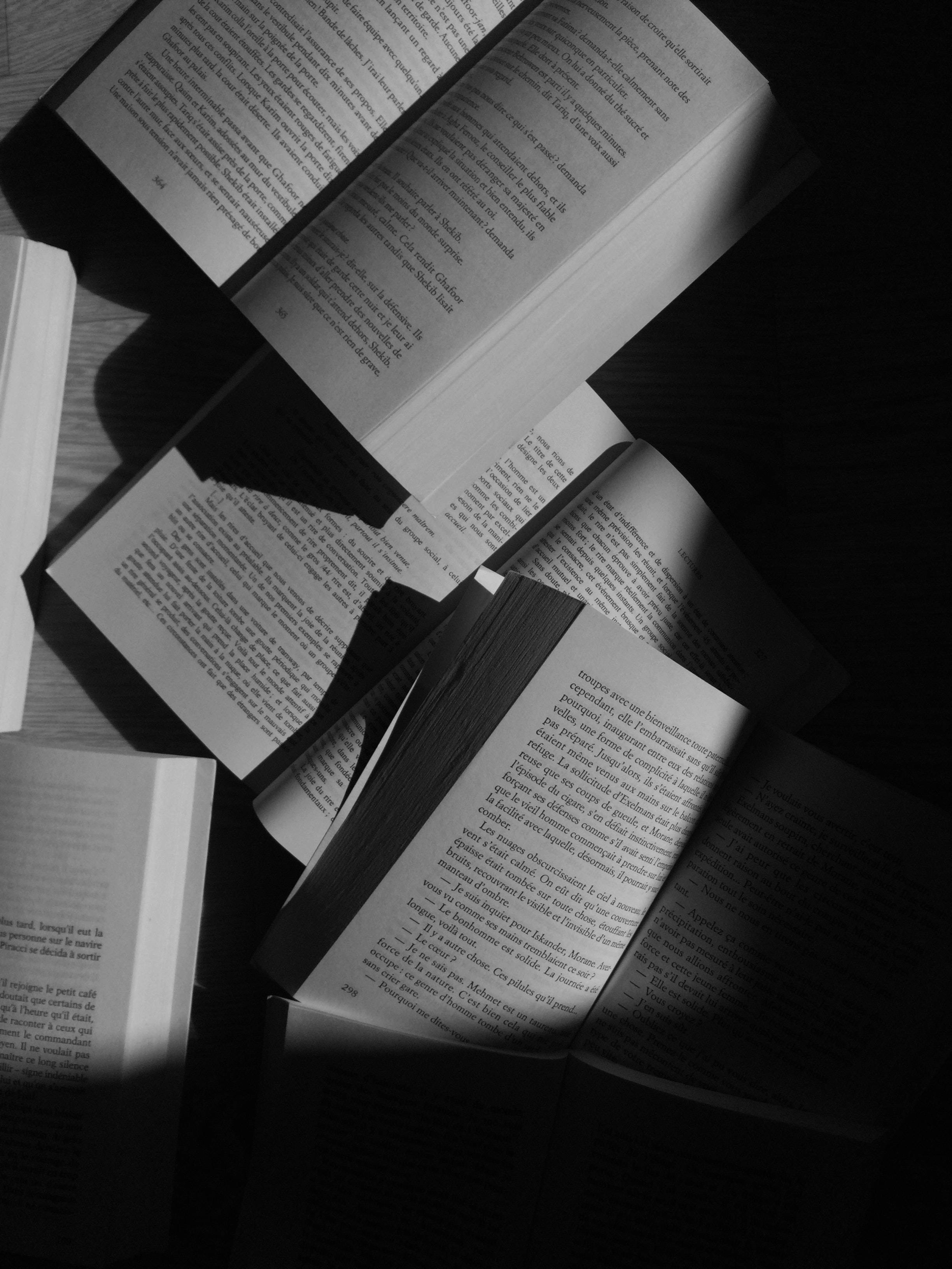 A black and white photo of several open books on a table. - Books