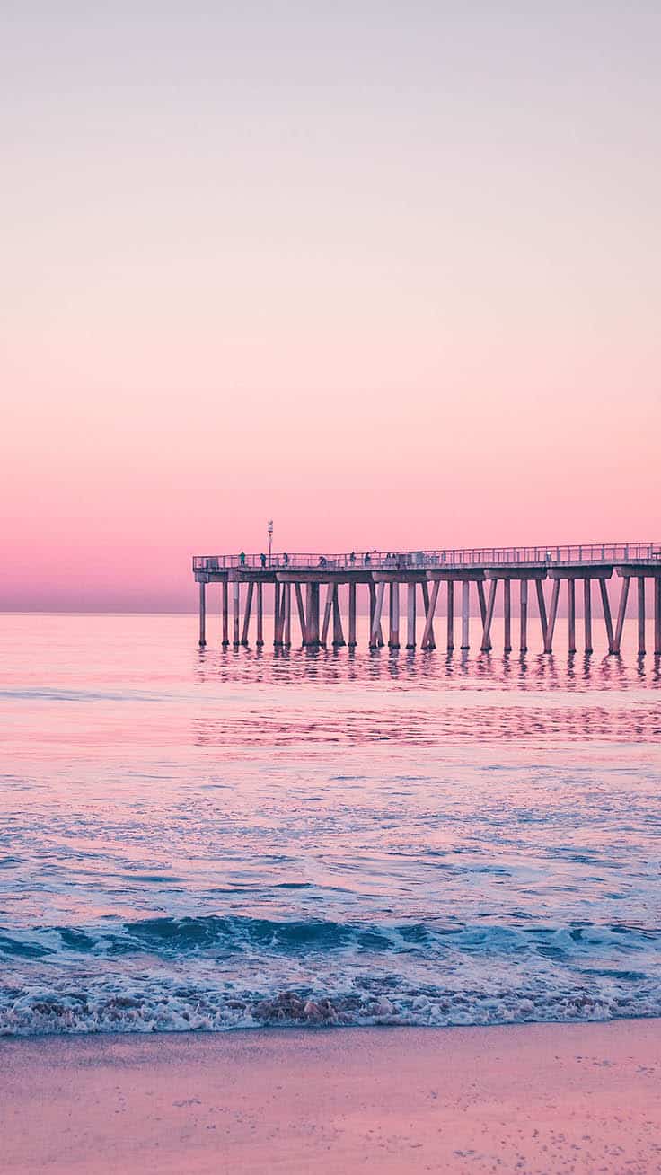 A long pier stretches out into the ocean during a pink sunset. - Calming