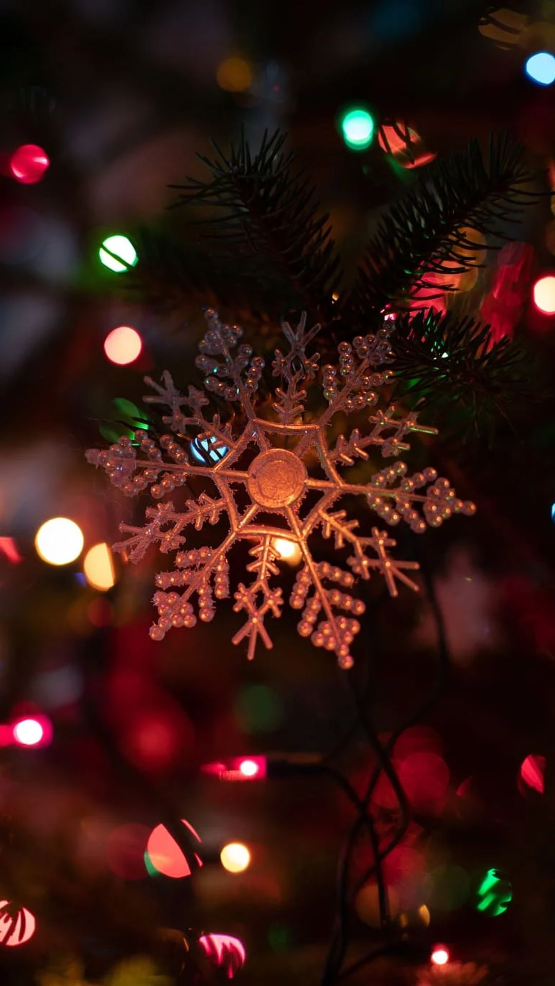 A close up of a snowflake ornament on a Christmas tree. - Christmas lights