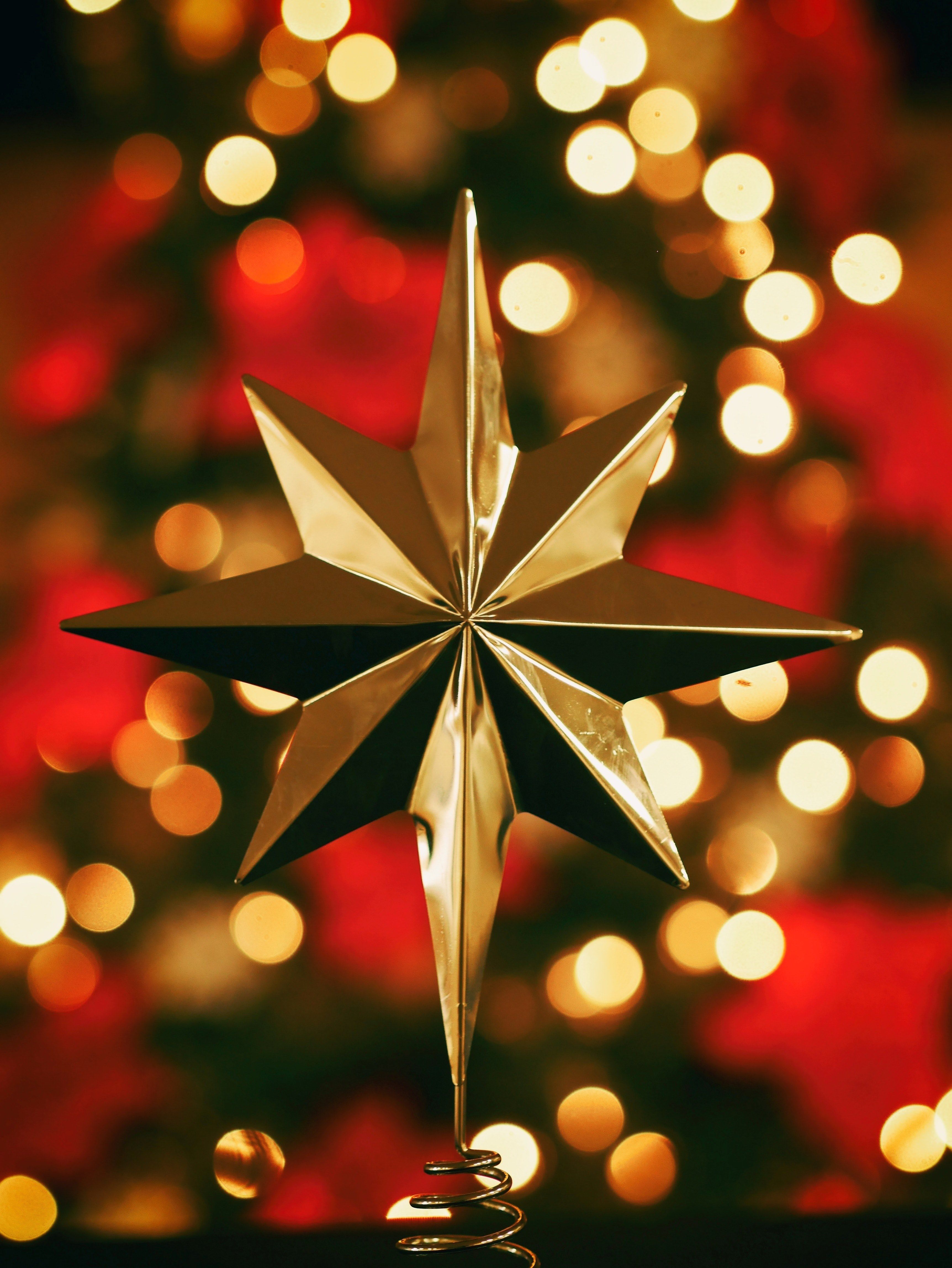 A gold star ornament on top of a Christmas tree. - Christmas lights