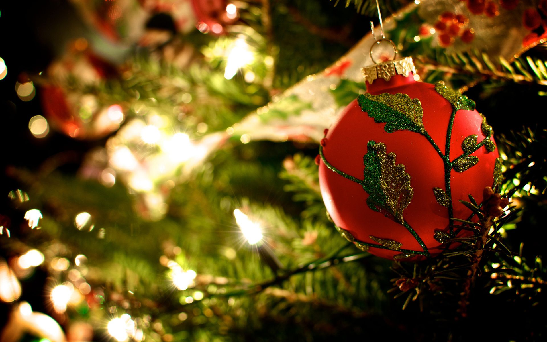 A red ornament with green leaves is hanging on a Christmas tree. - Christmas lights