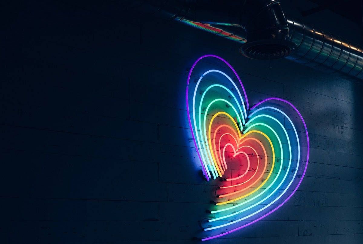 A neon sign of a heart in rainbow colors on a dark background. - Heart