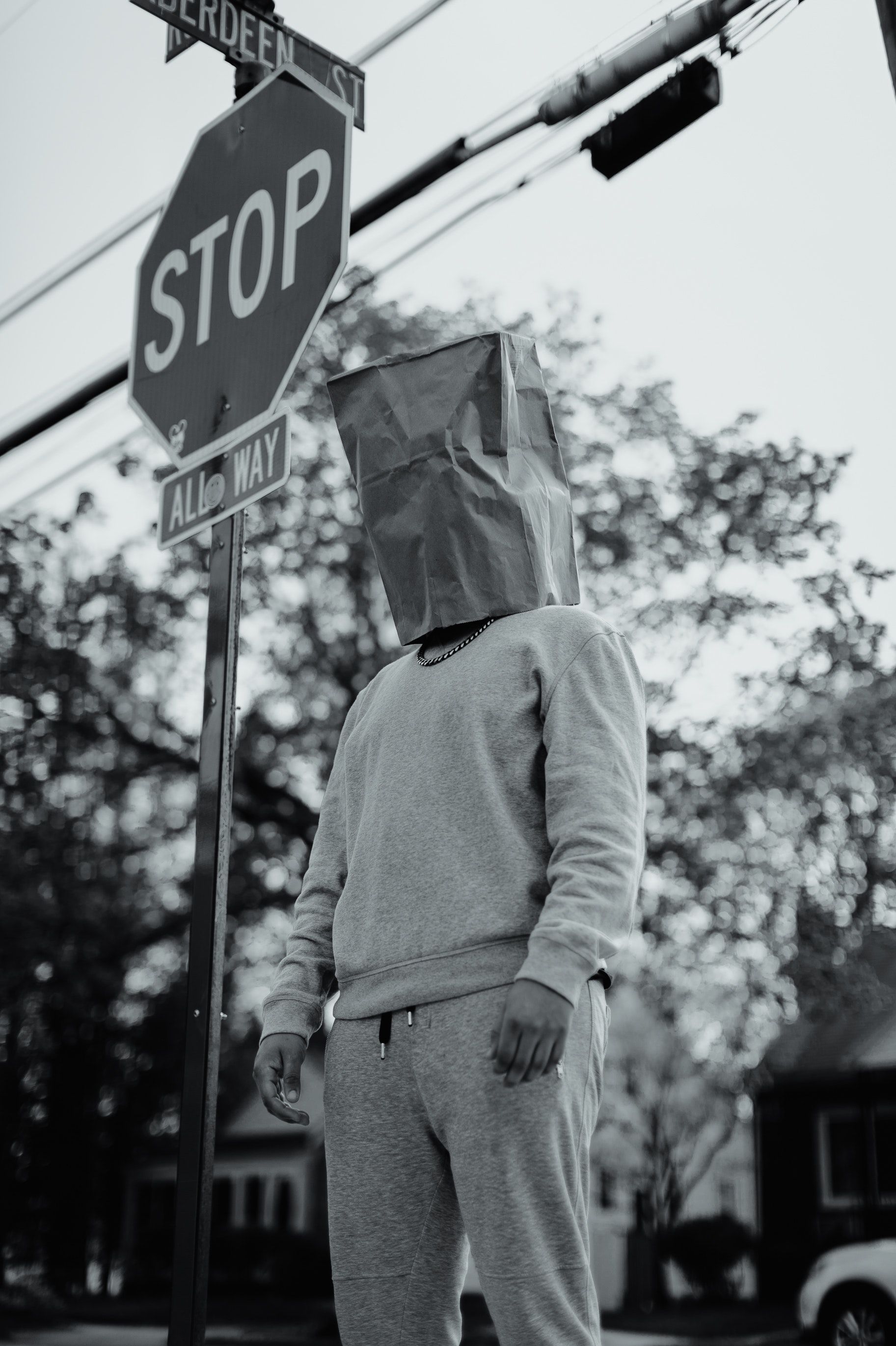 Grayscale photo of man wearing bag over his head standing beside stop sign - Trippy