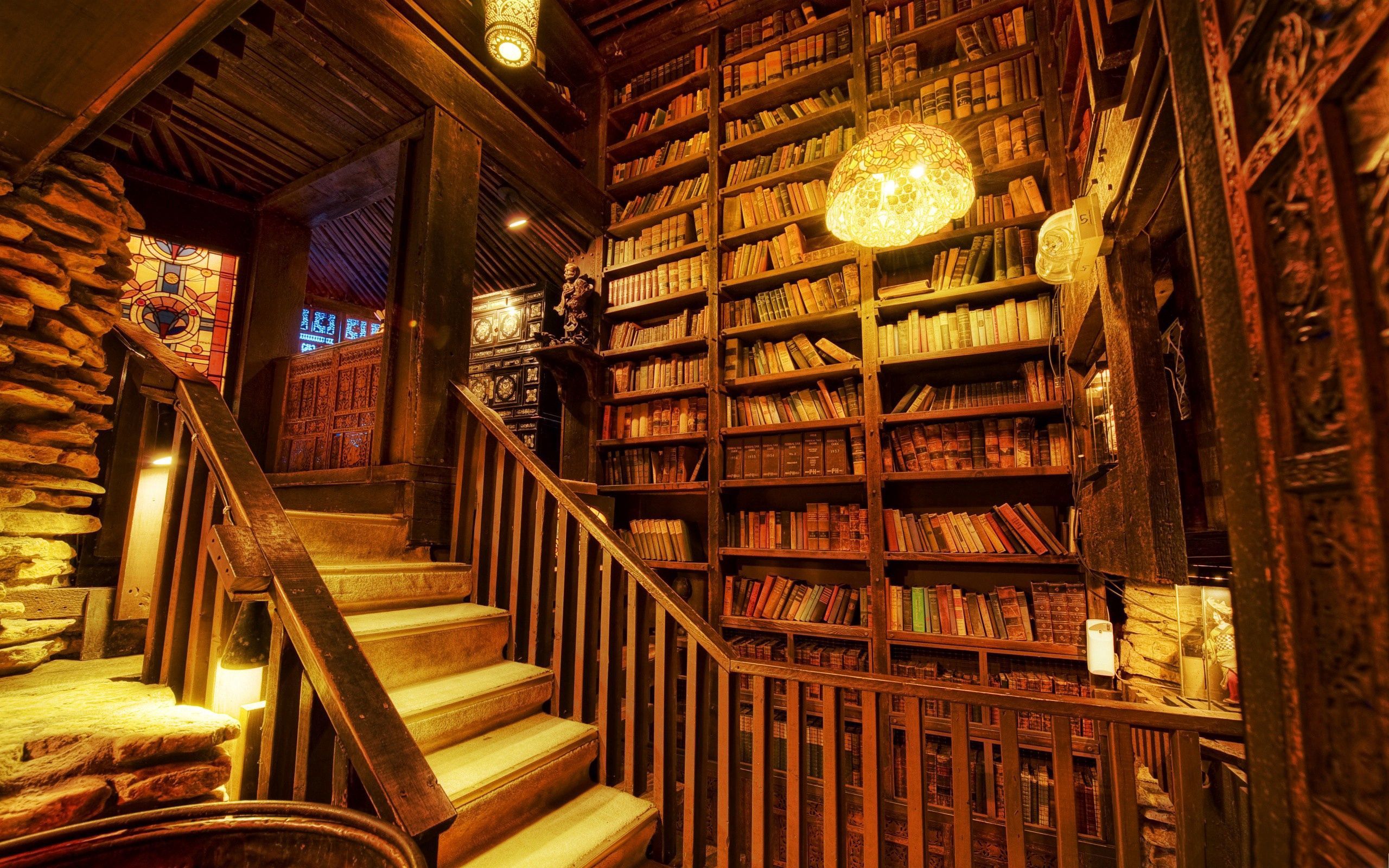 A library with a wooden staircase and bookshelves full of books. - Library