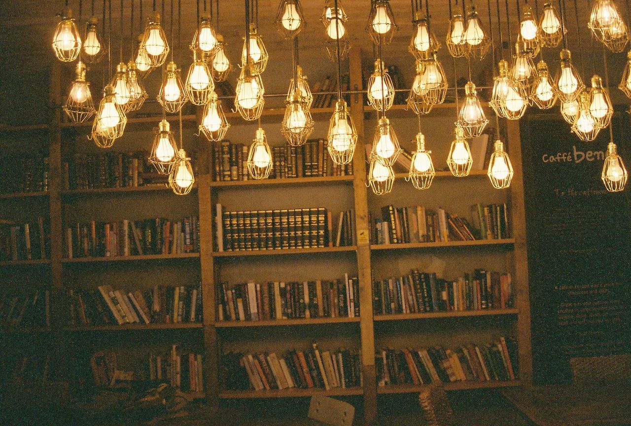 A room with bookshelves and hanging lightbulbs - Library