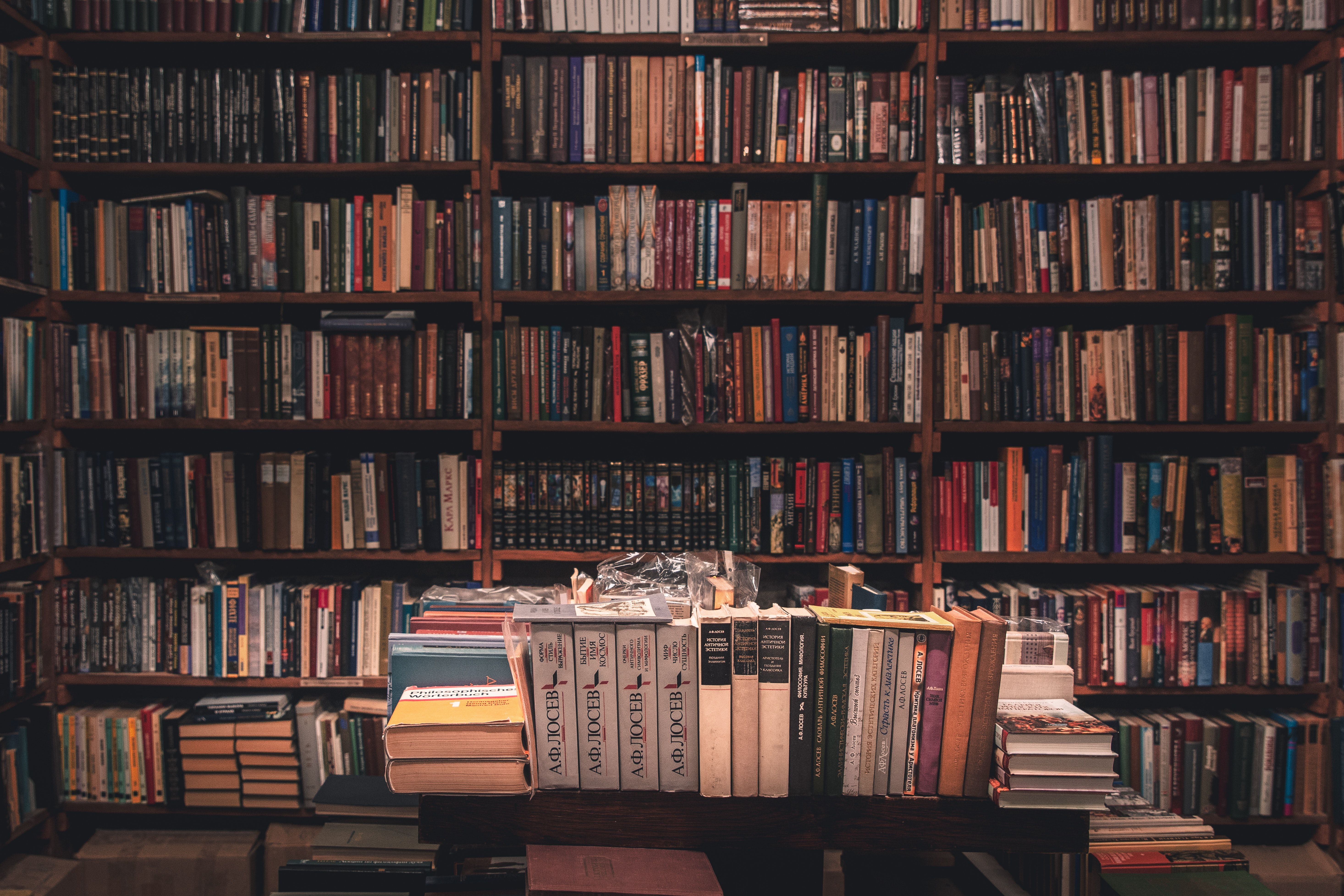 A table with a few books on it, in front of a bookshelf full of books. - Library