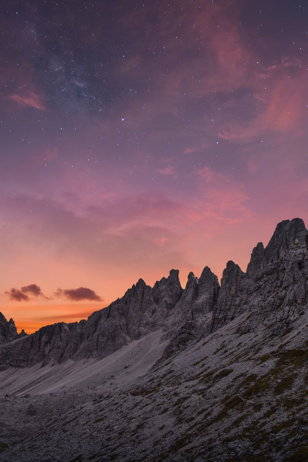 The sky is painted with a beautiful purple and orange color as the sun sets behind the rocky mountain. - Rocks