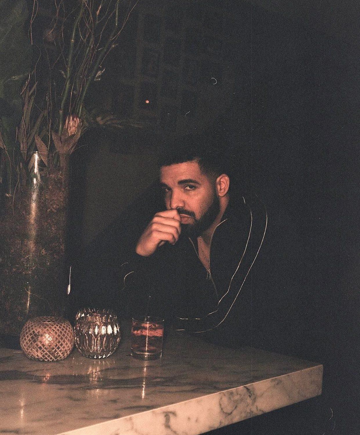 A man sitting at the bar in front of some glasses - Drake