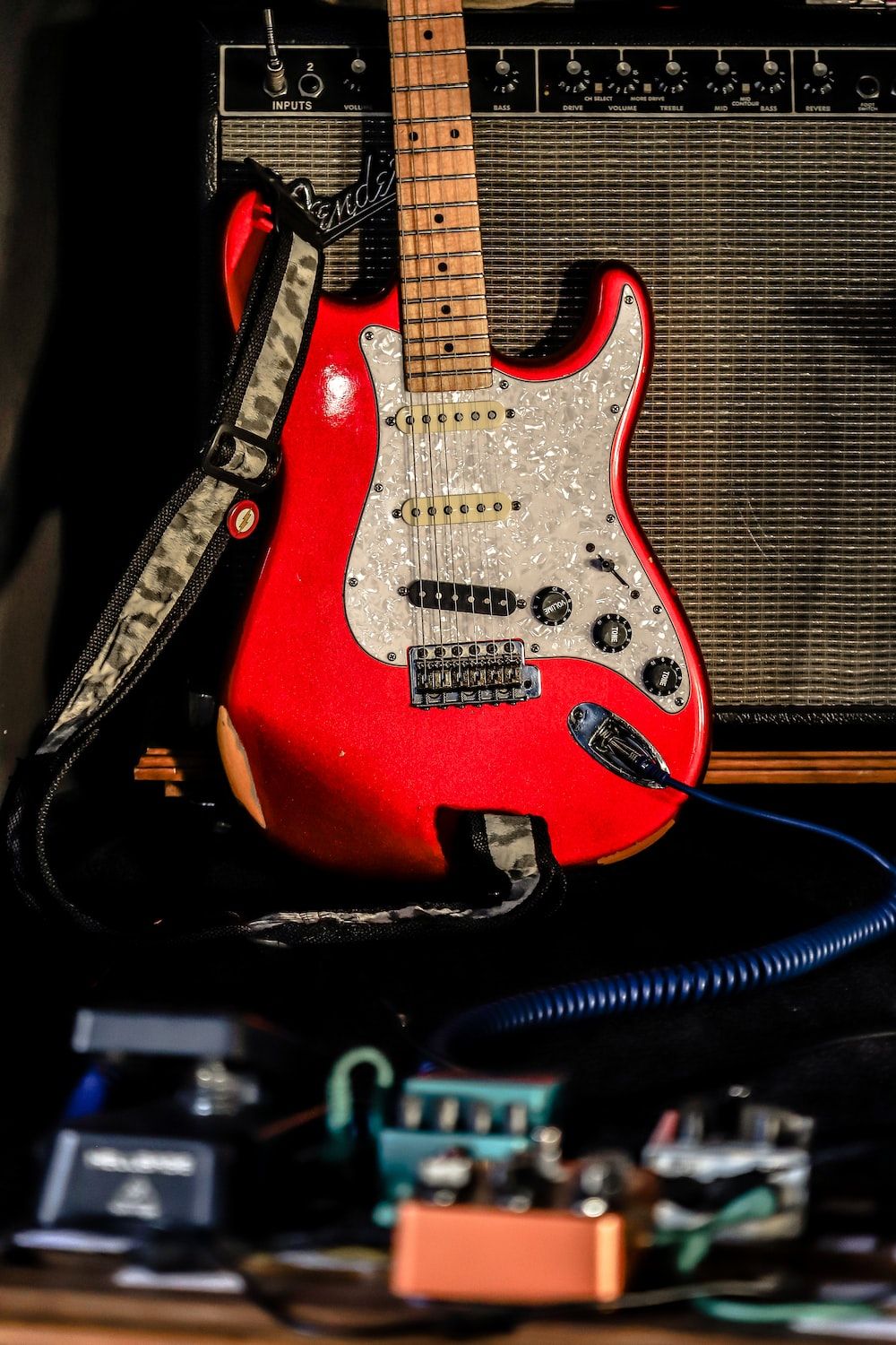 A red electric guitar sitting on a black guitar case in front of a black amplifier. - Guitar