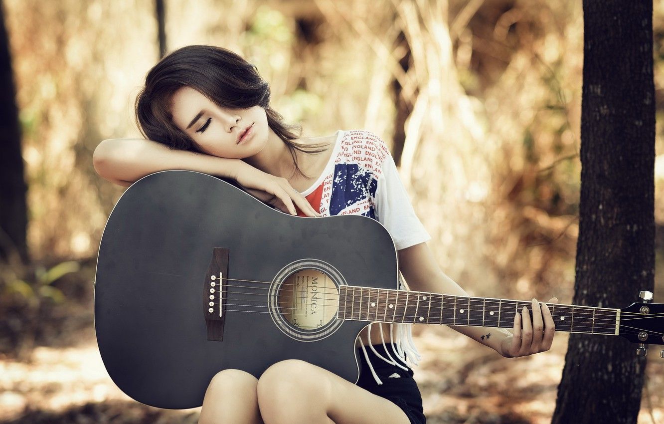A woman sitting in the woods with an acoustic guitar - Guitar