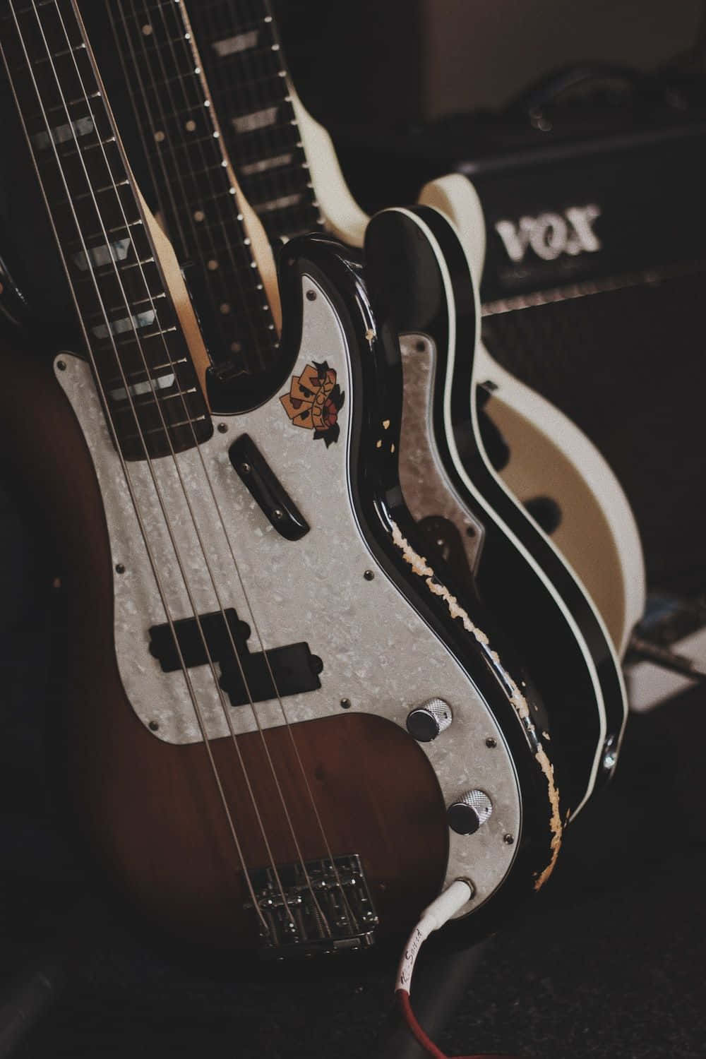 A close up of two bass guitars in front of a Vox amplifier. - Guitar