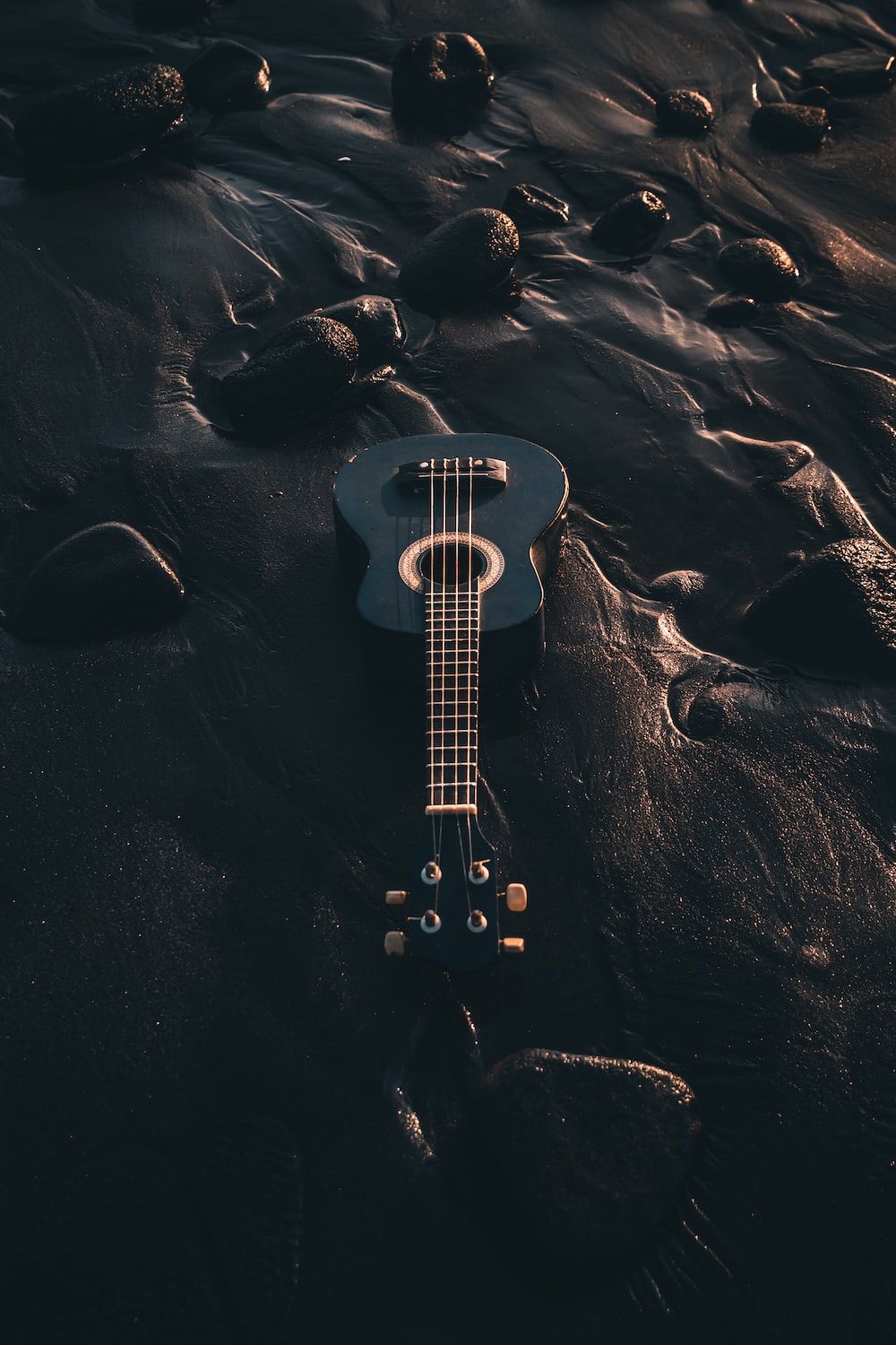 A guitar laying on the beach in front of rocks - Guitar