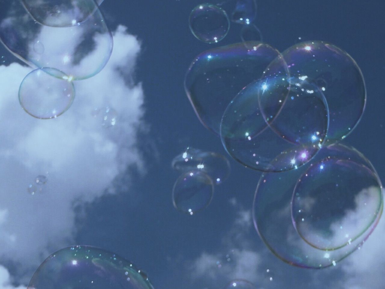 Bubbles floating in the air with a blue sky and white clouds in the background. - Bubbles