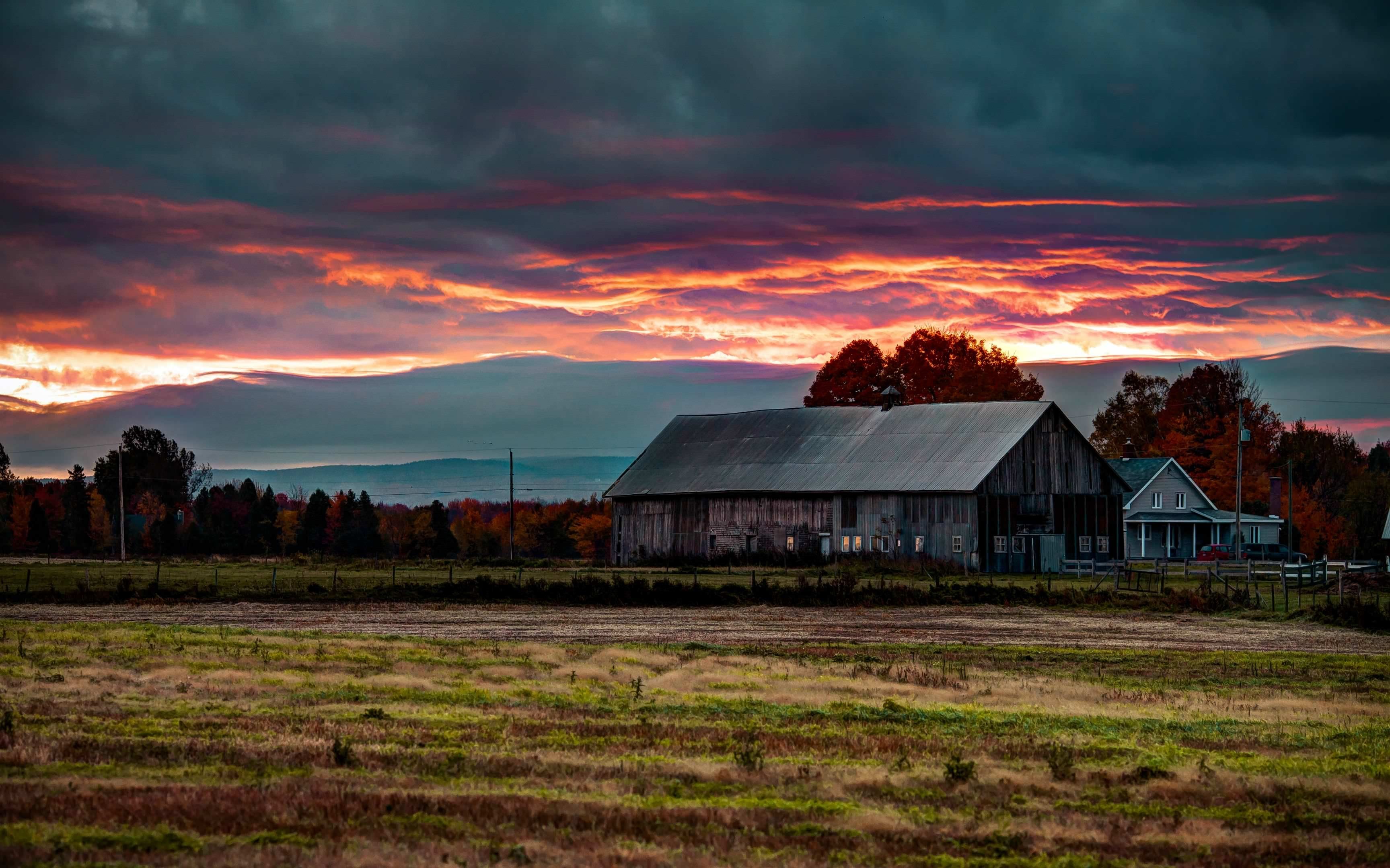 A barn sits in a field with a dramatic sunset in the background. - Farm
