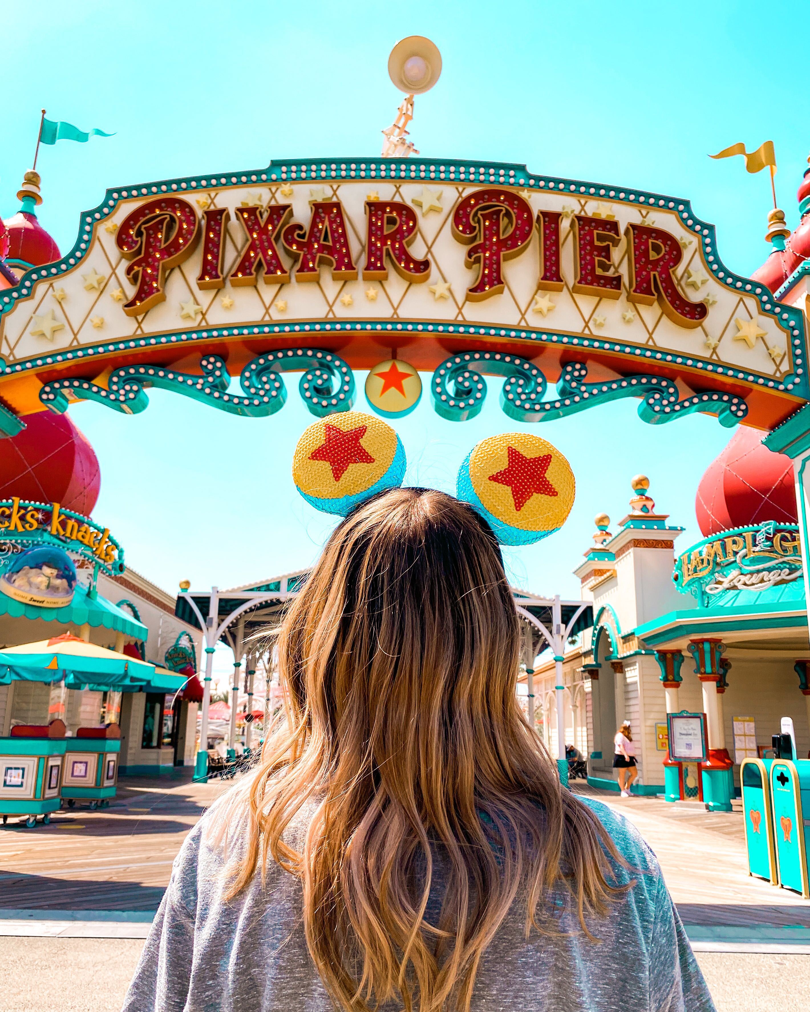 The entrance to Pixar Pier with a girl standing in front of it - Disneyland