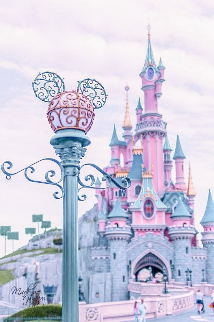 A pink castle with people walking around it - Disneyland