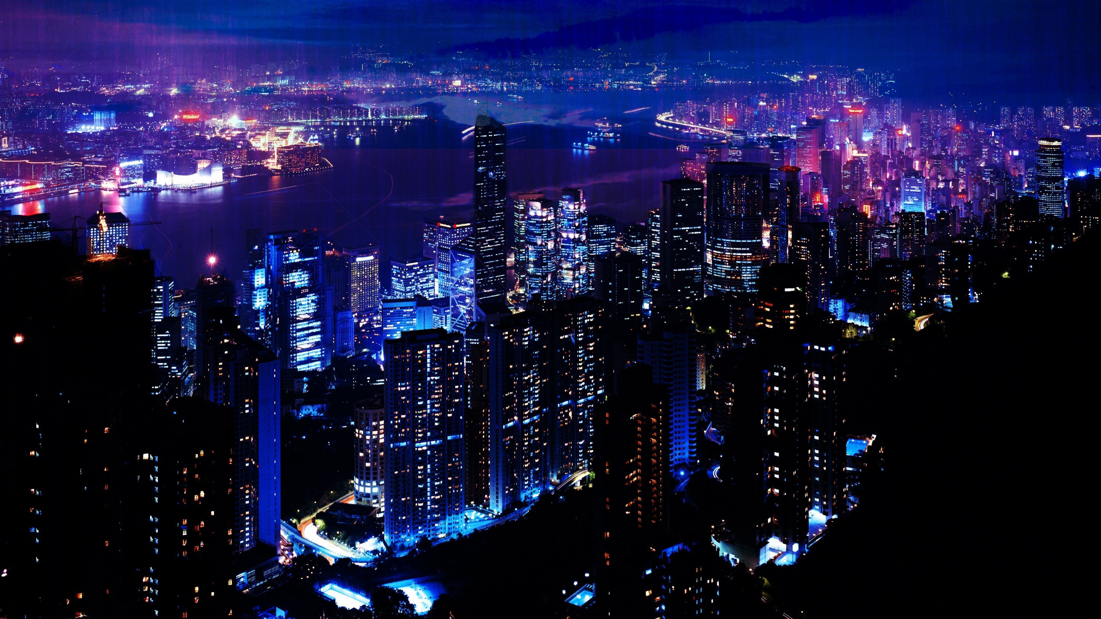 A cityscape at night with bright blue and purple lights illuminating the buildings. - 3840x2160