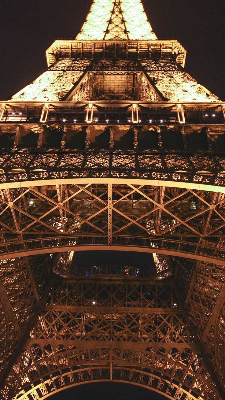 The bottom of the Eiffel Tower is lit up at night. - Gold