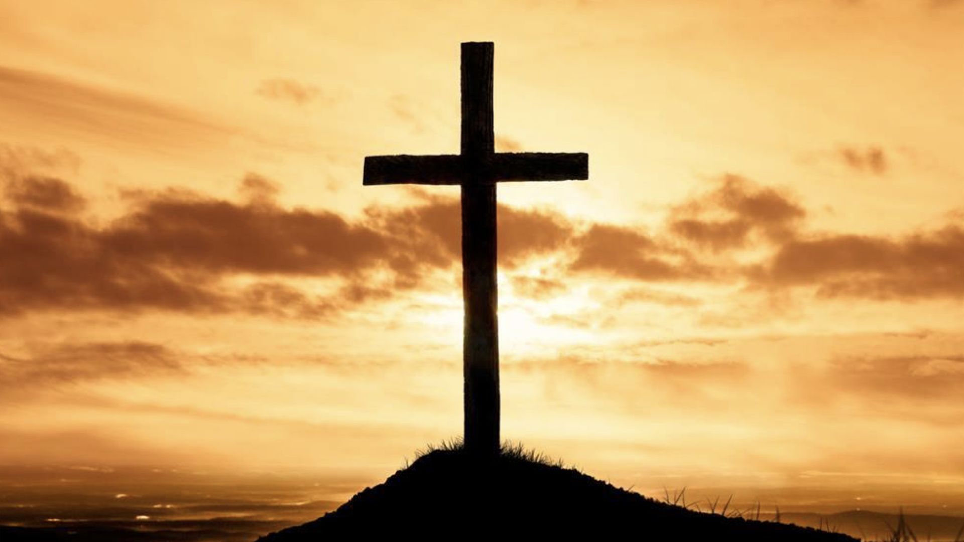 A silhouette of a cross on a hill at sunset. - Cross