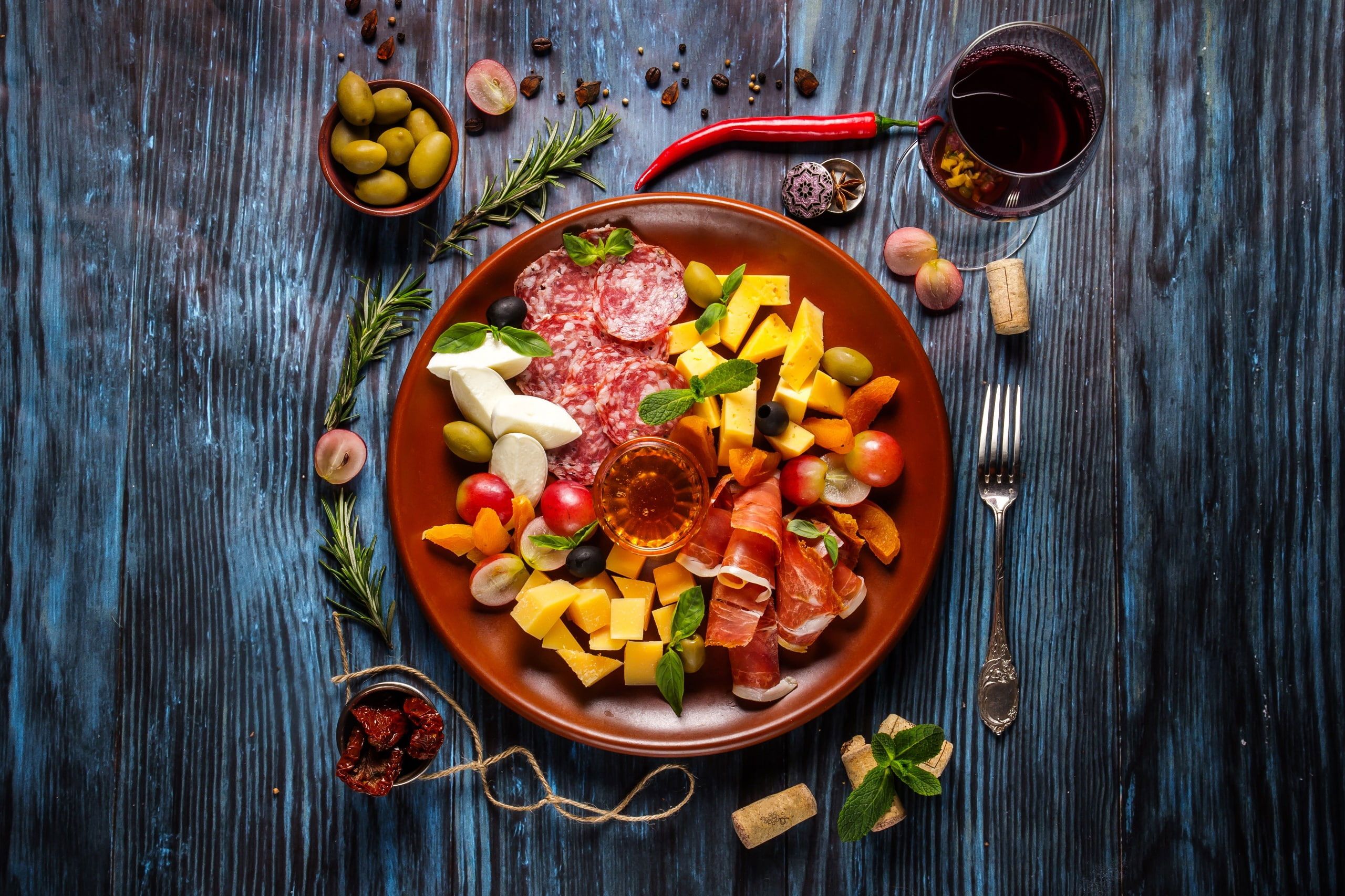 A plate of assorted meats, cheeses, and fruits with a glass of wine. - Foodie