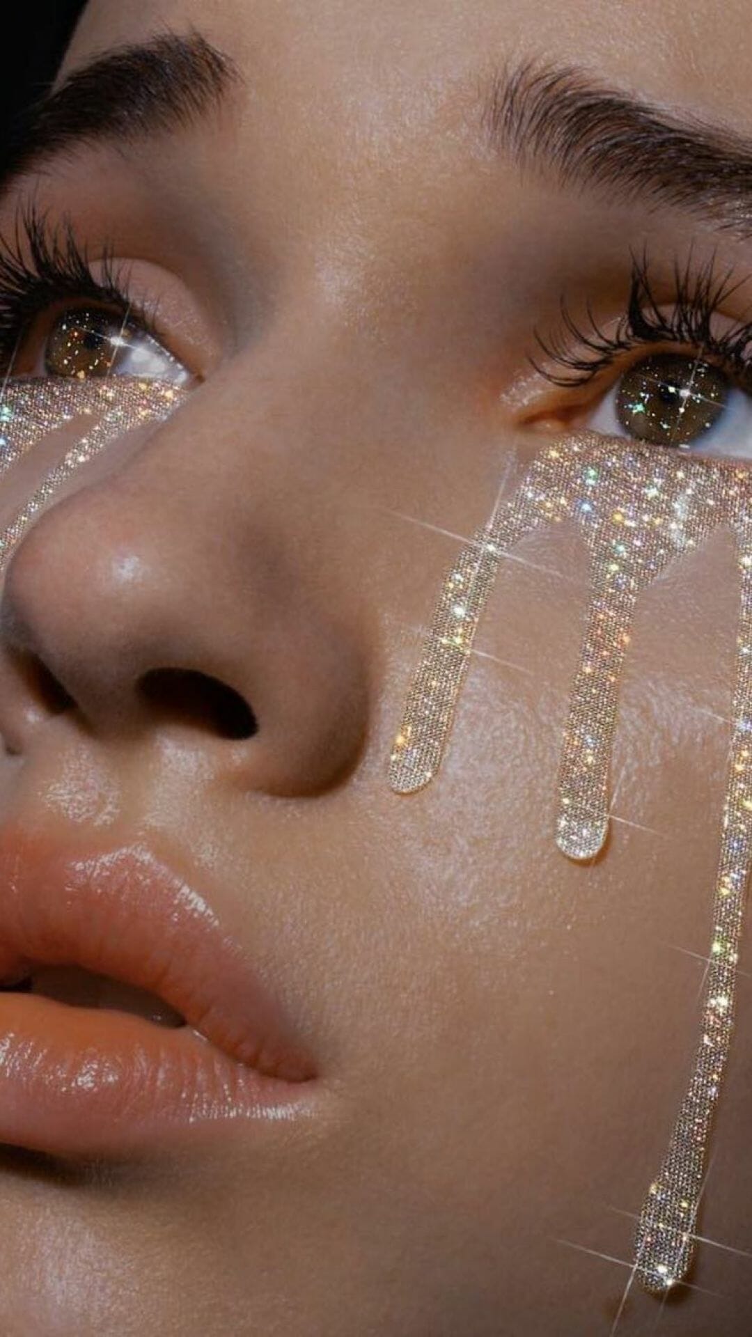 A model with gold glitter on her face and gold eye shadow. - Eyes, glitter