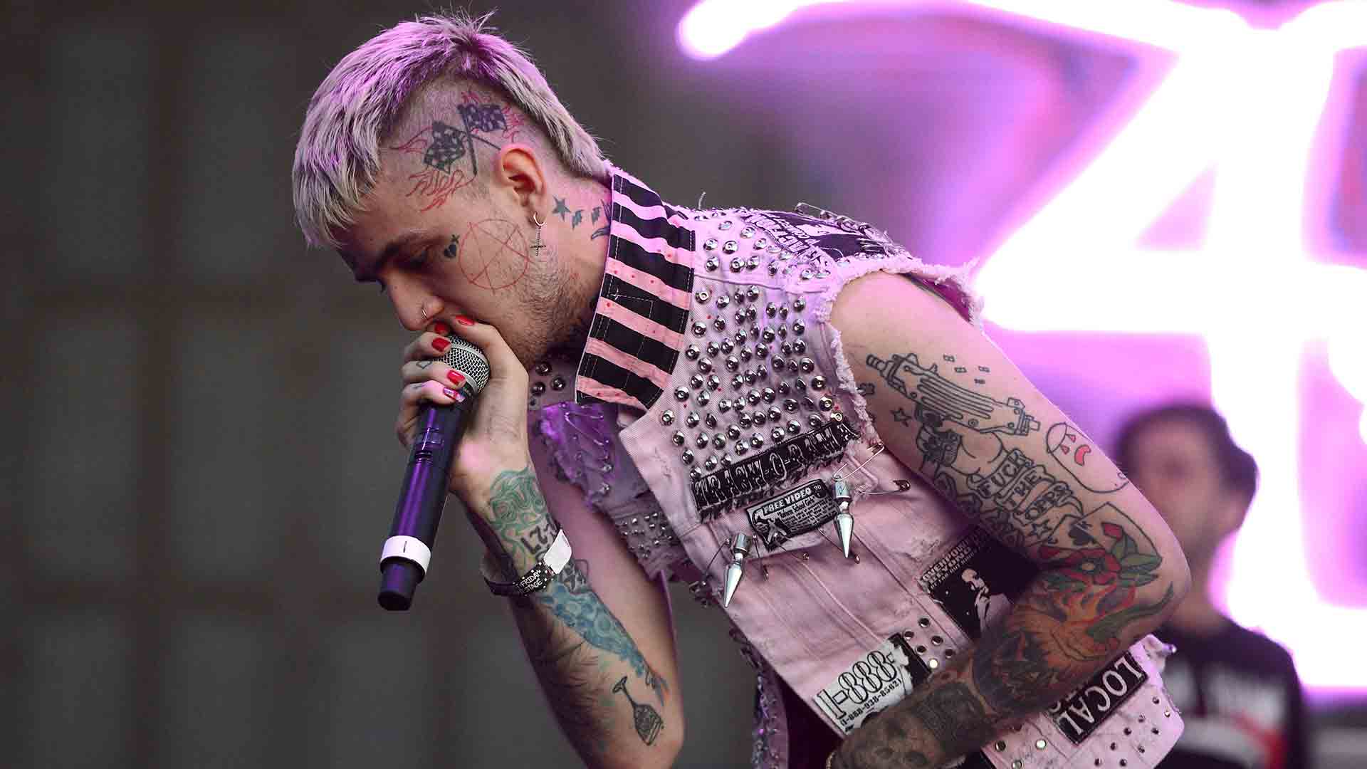 A man with tattoos on his arms and neck singing into microphone - Lil Peep