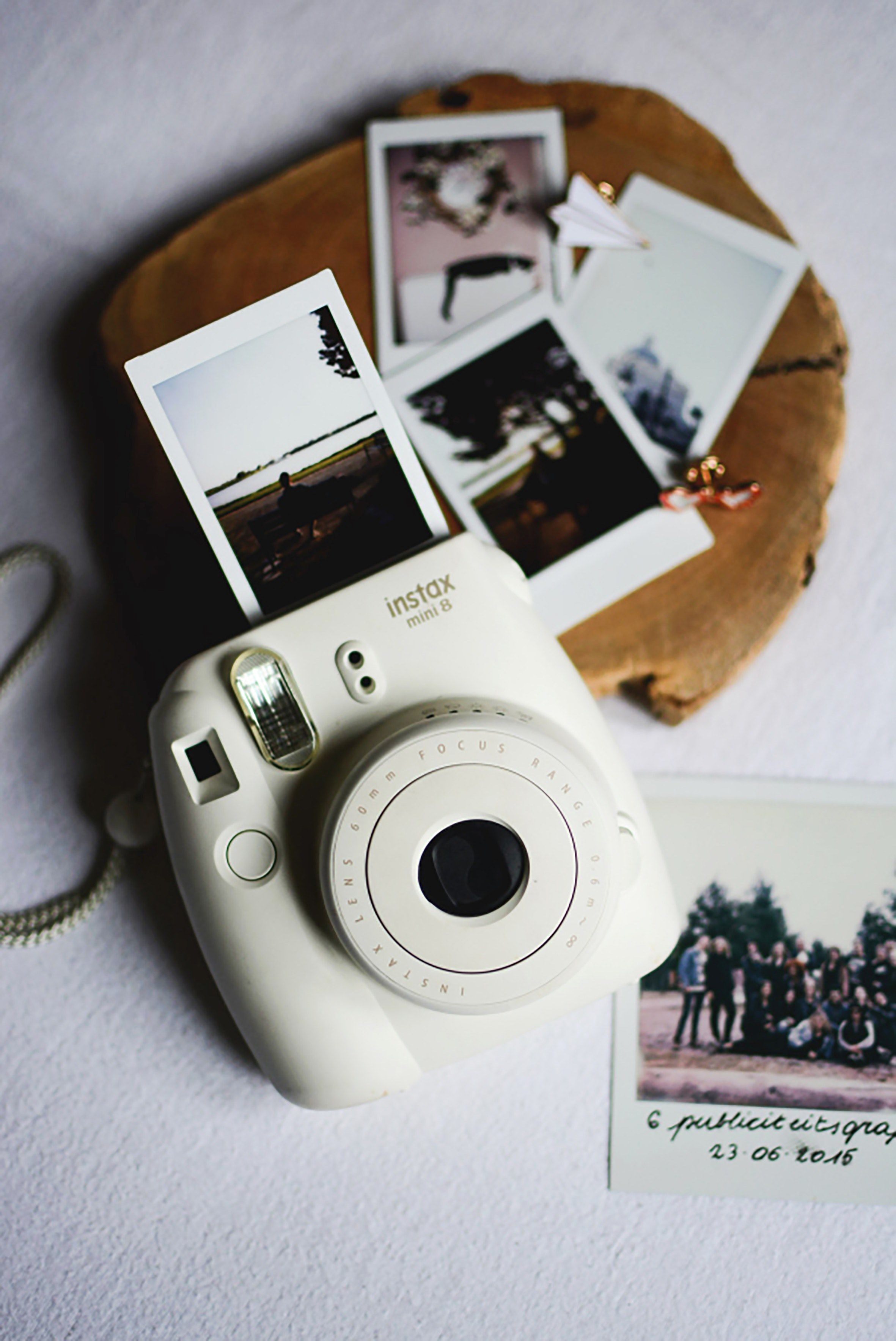 A white instant camera with polaroid photos on a wooden board - Polaroid