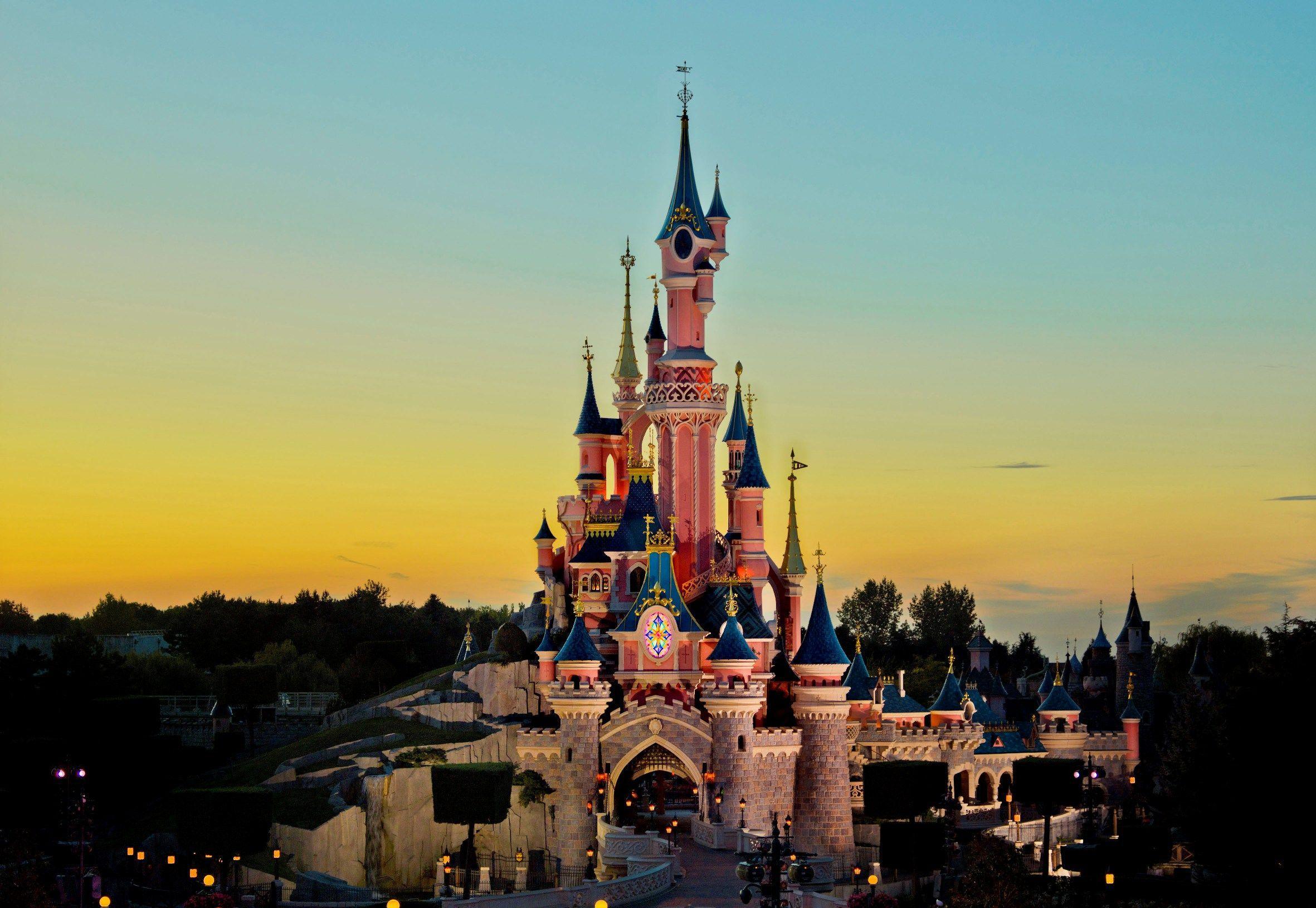 The Sleeping Beauty Castle at Disneyland Paris is lit up at night with a blue and pink glow. - Disneyland