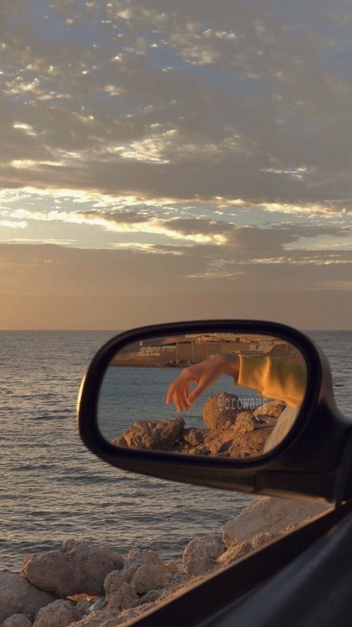 A person's hand is reflected in the side mirror of a car. - Sunset