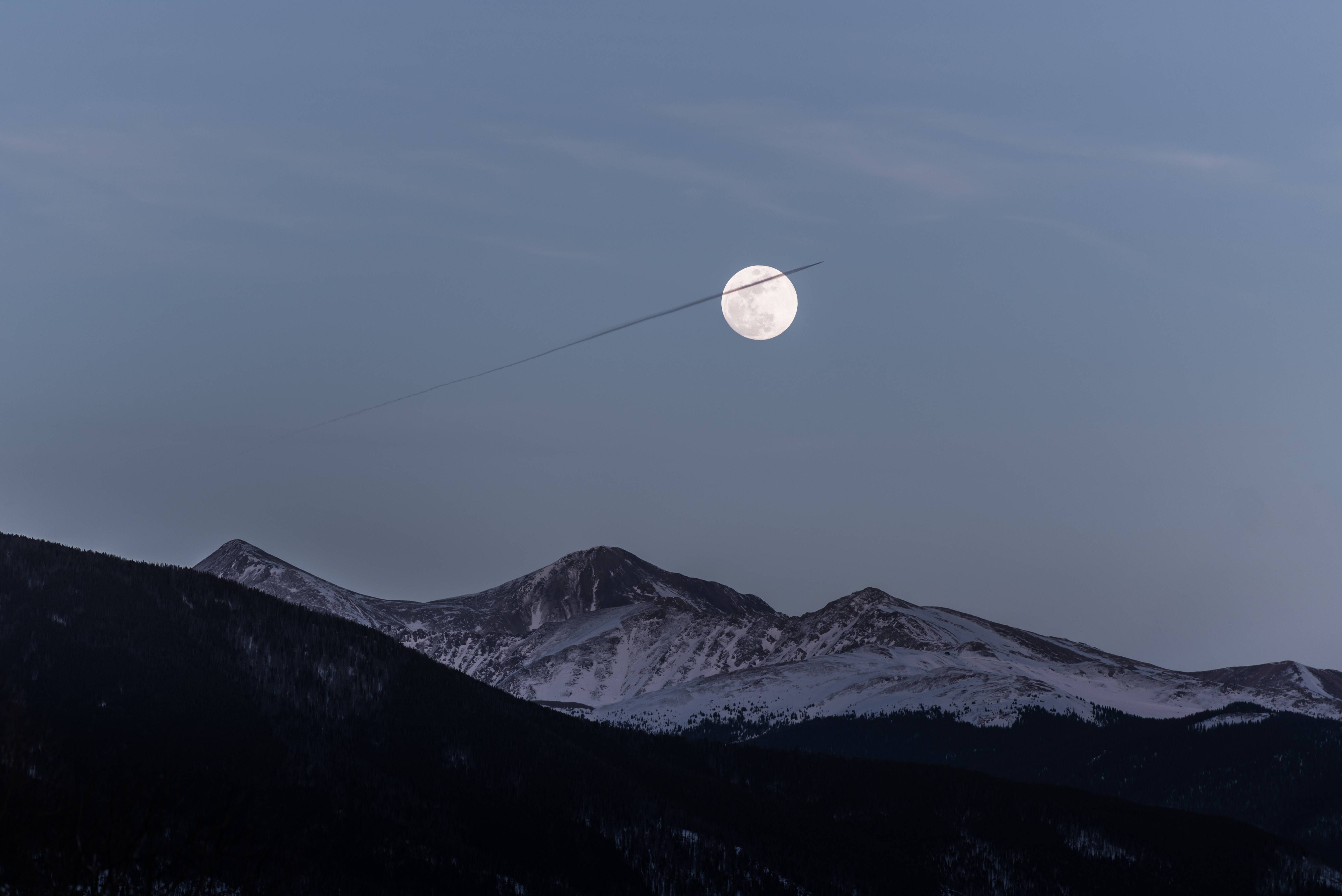 A full moon rising over a snow-covered mountain range. - Mountain