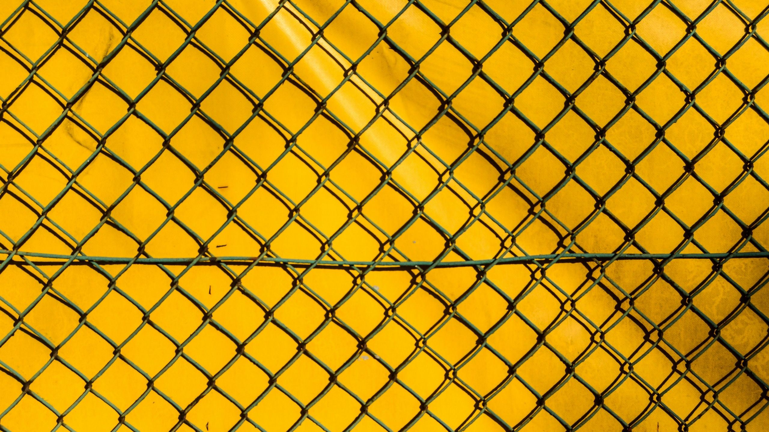 A yellow wall with a chain link fence in front of it - Grid