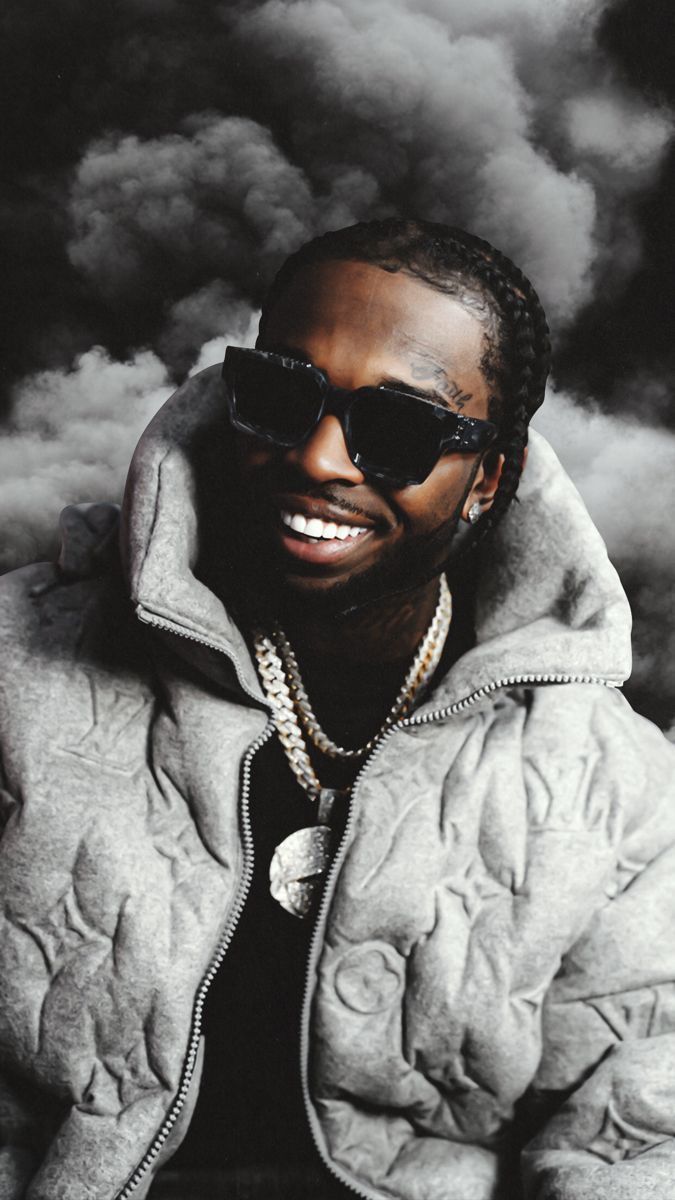A grey scale image of a smiling man wearing a grey coat and sunglasses. - Pop Smoke