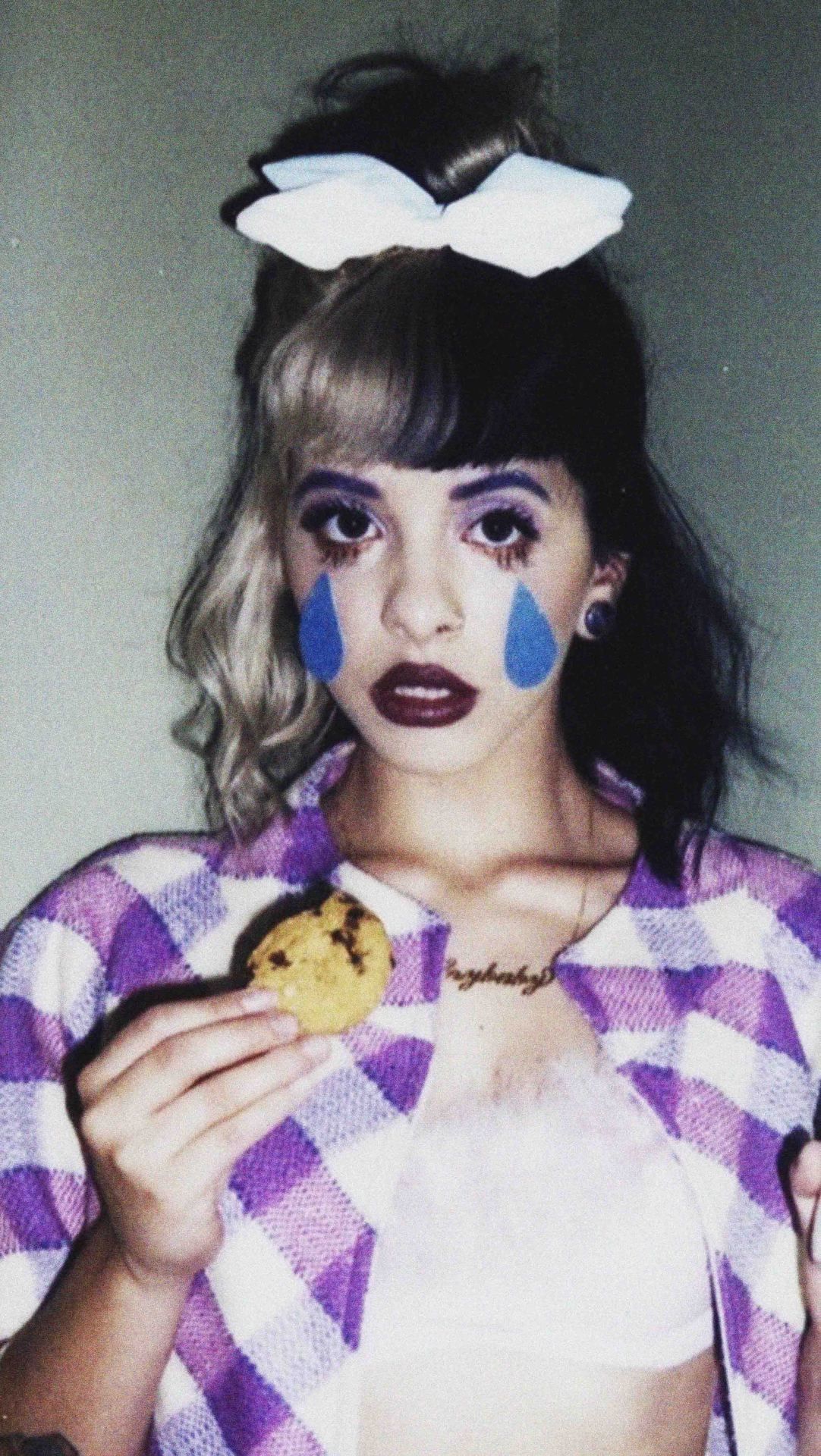 A girl with a bow in her hair and makeup that makes her look like she's crying while eating a cookie - Melanie Martinez