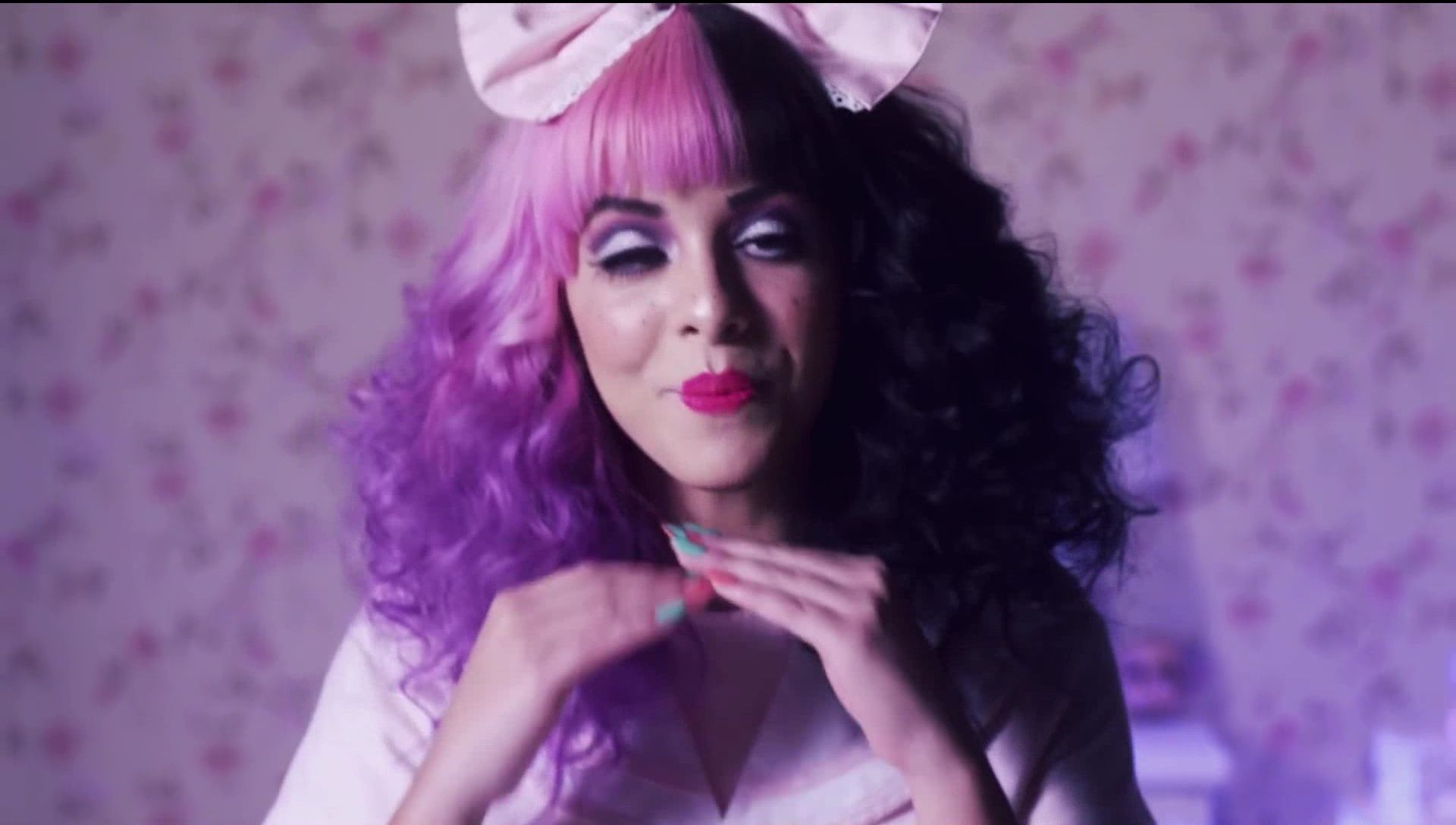 A woman with pink hair and a pink bow in her hair. - Melanie Martinez