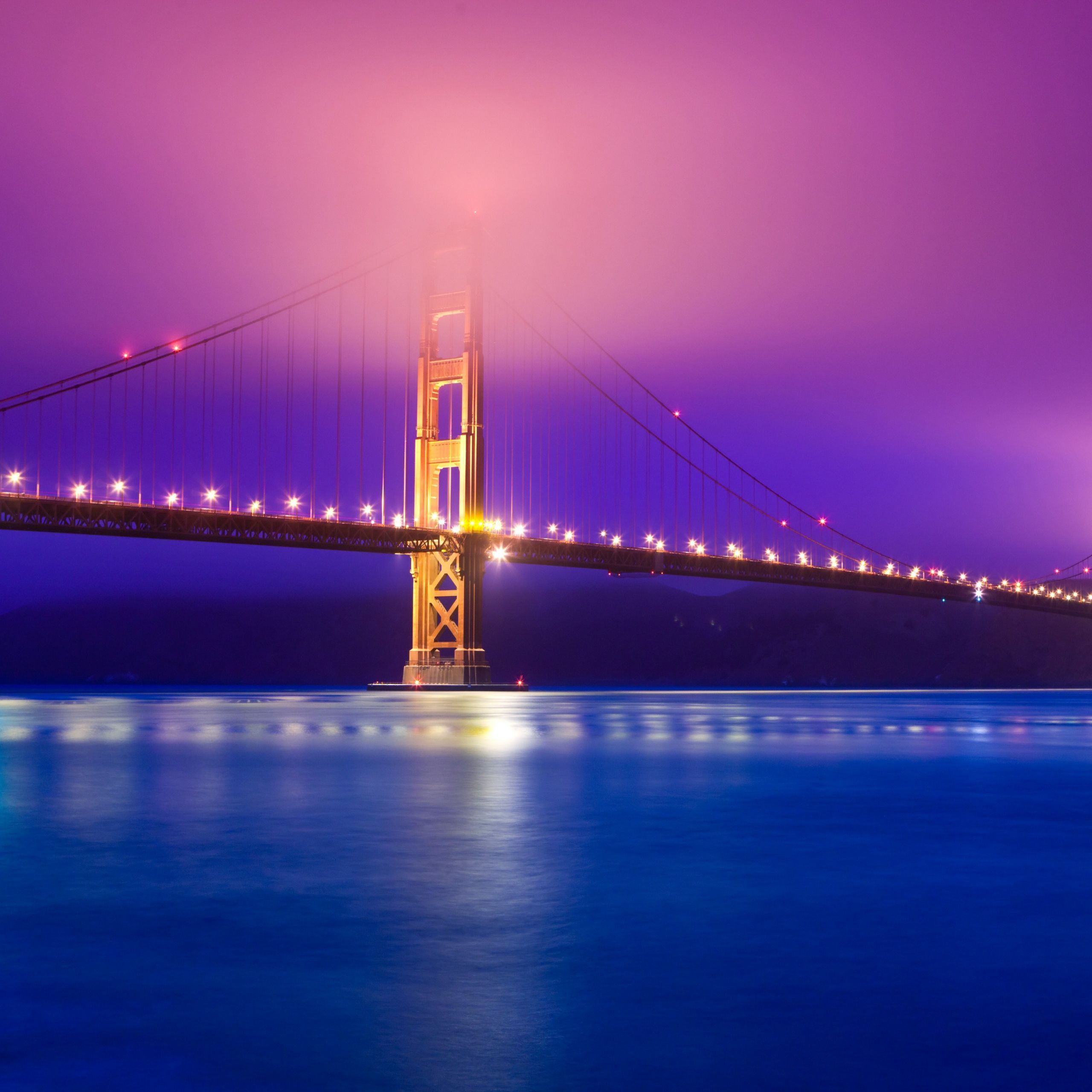 The Golden Gate Bridge is illuminated at night with a purple sky. - California