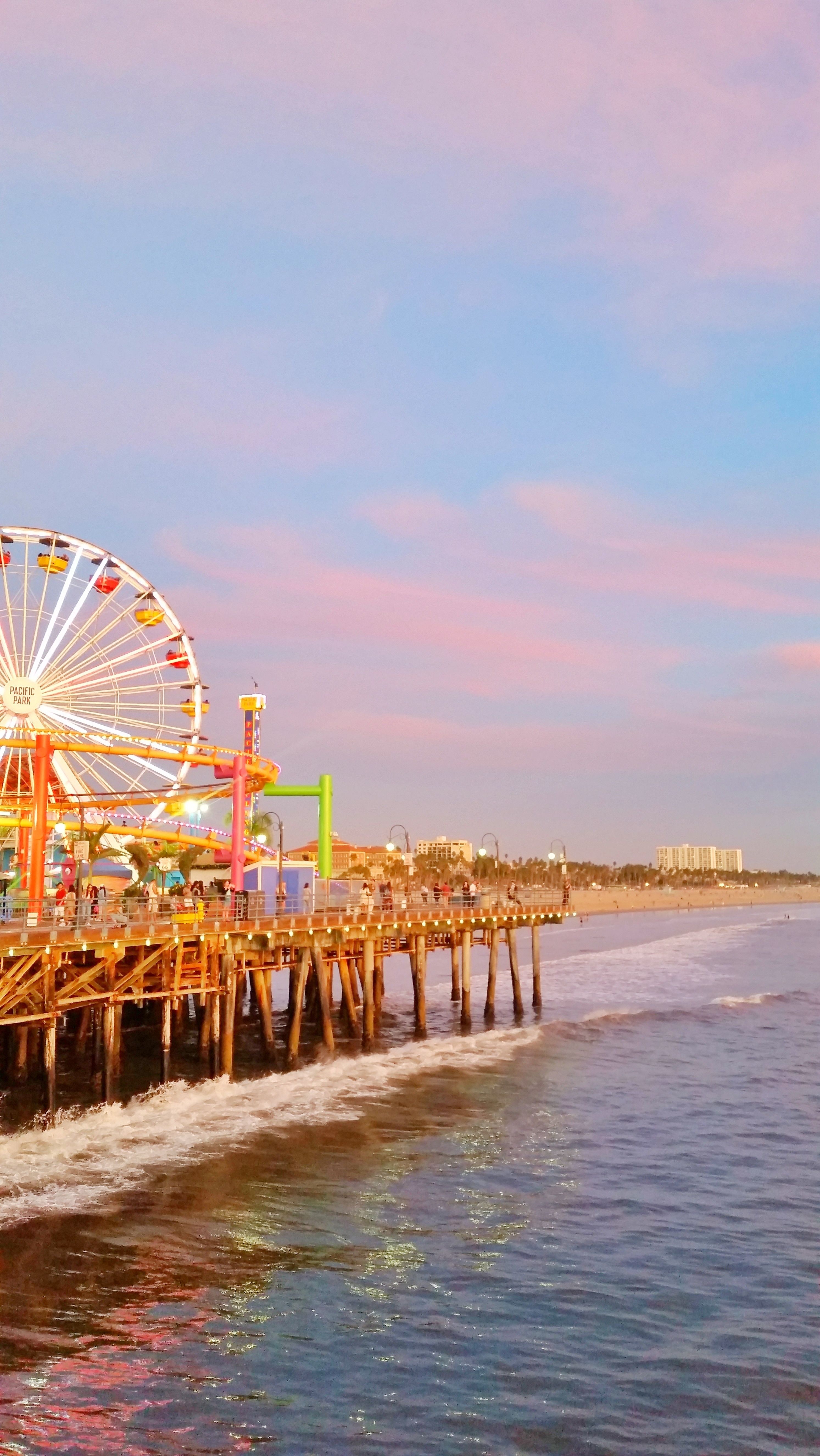 A colorful ferris wheel sits on a pier in the ocean. - California