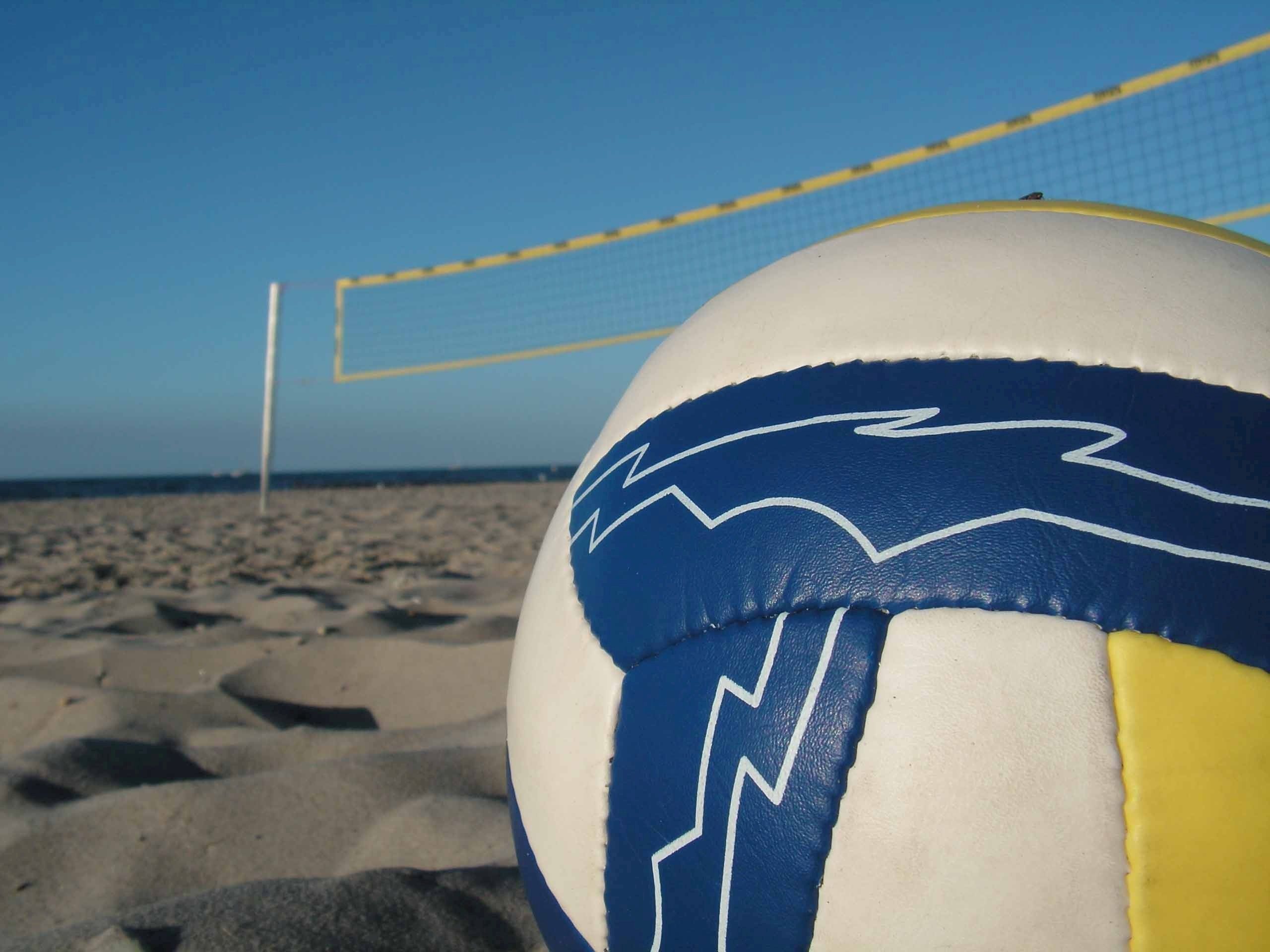 A volleyball on the beach in front of a volleyball net. - Volleyball