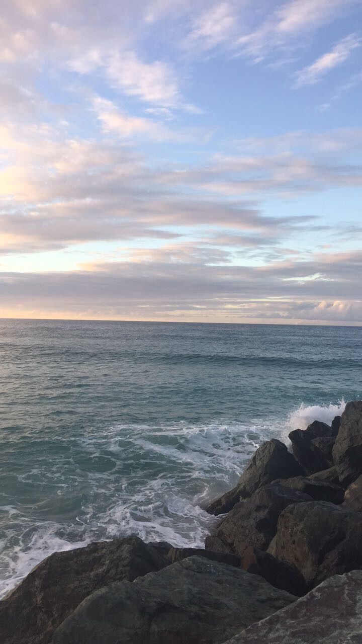 A man standing on the rocks looking at water - Travel