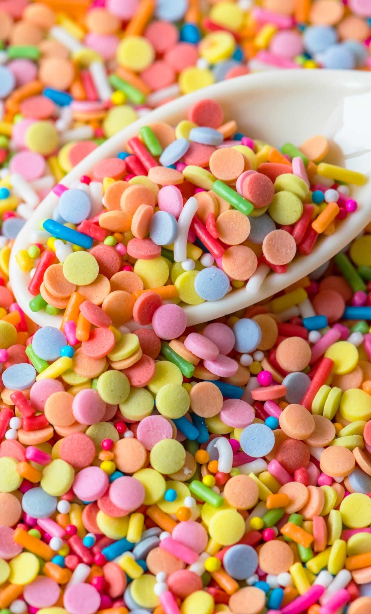 A close up of a spoonful of brightly colored sprinkles. - Candy