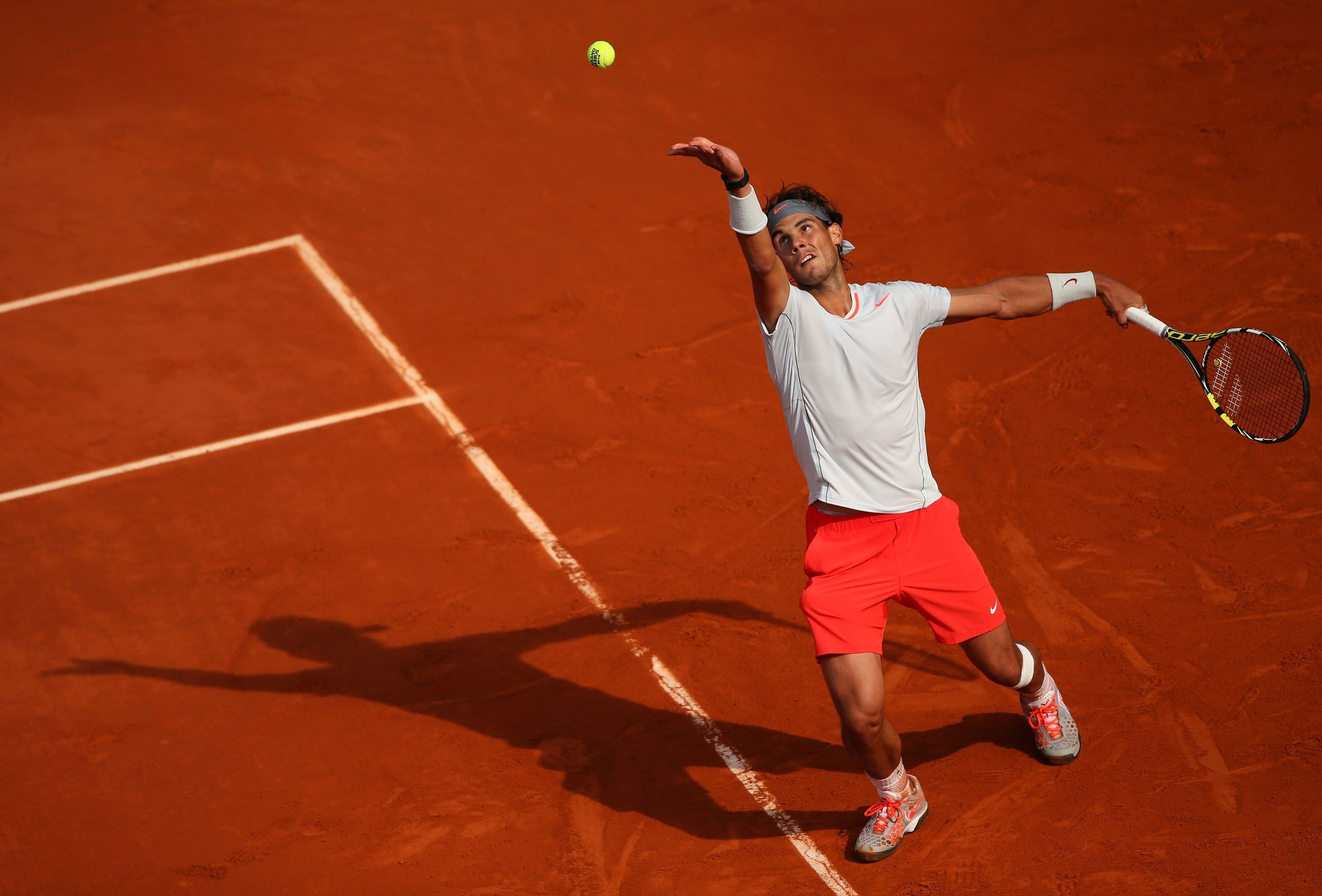 A tennis player serving the ball on a clay court. - Tennis