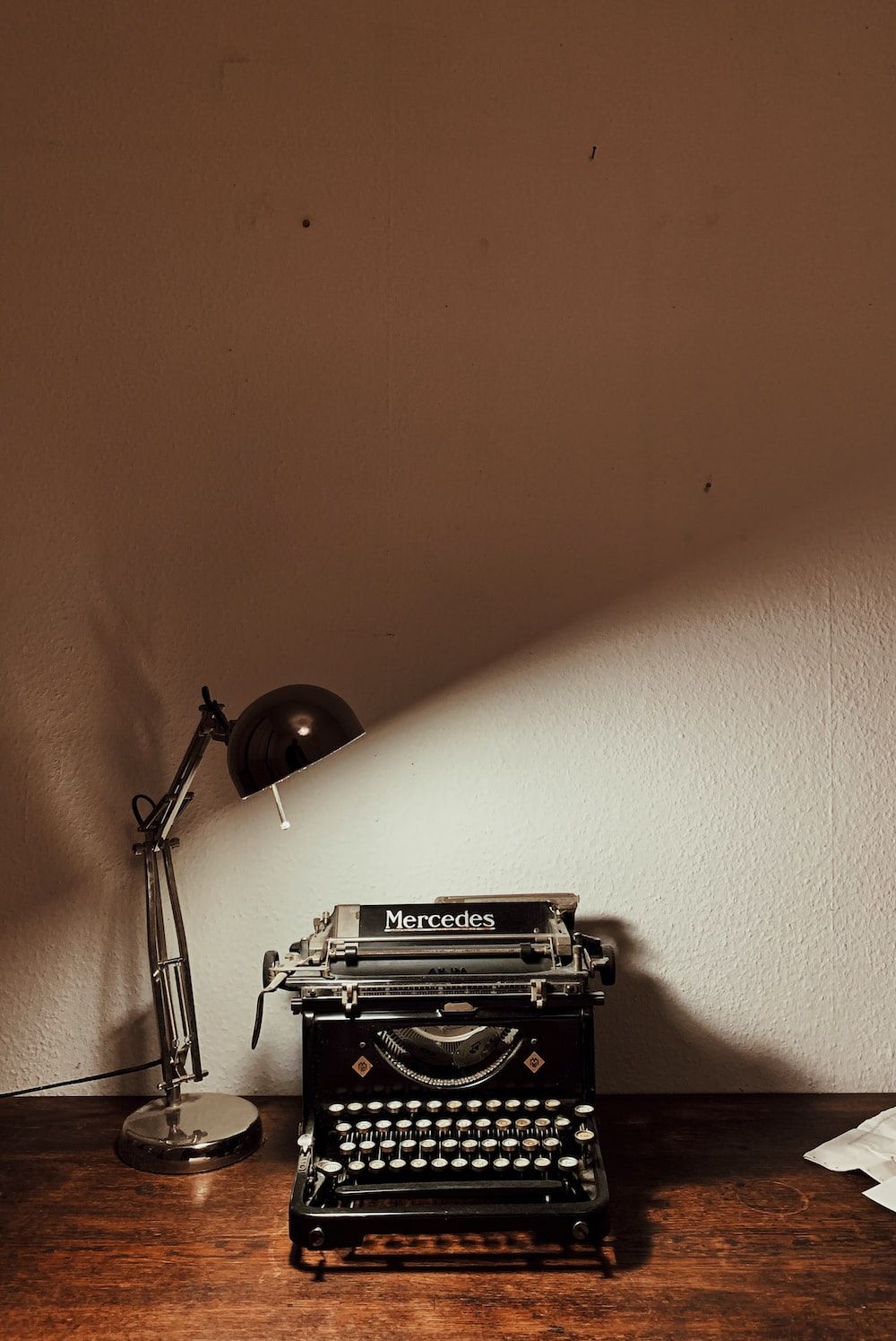 A black typewriter with the word Mercedes on it sits on a wooden table next to a lamp. - Brown, light brown