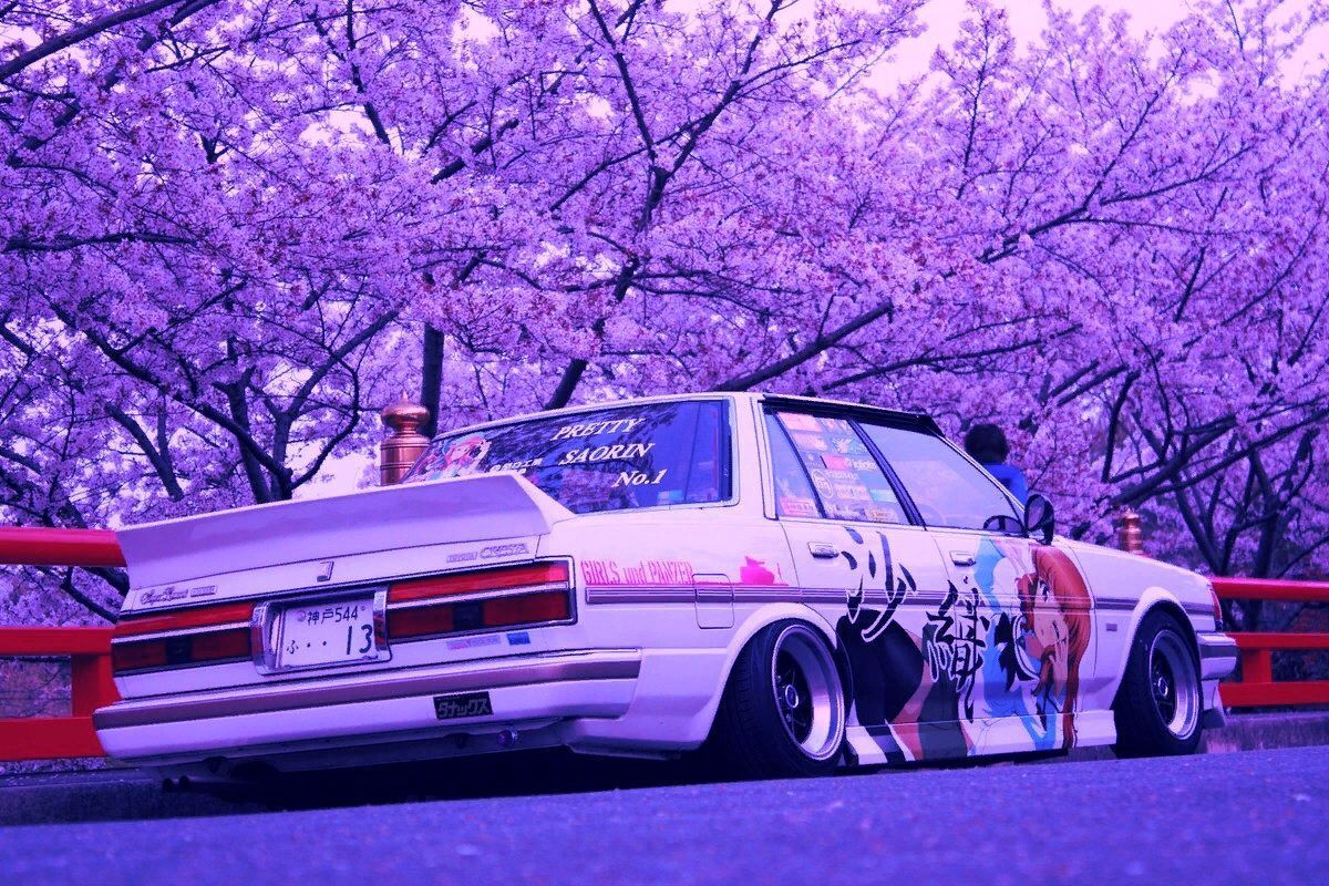 A car with anime stickers parked under cherry blossom trees - JDM