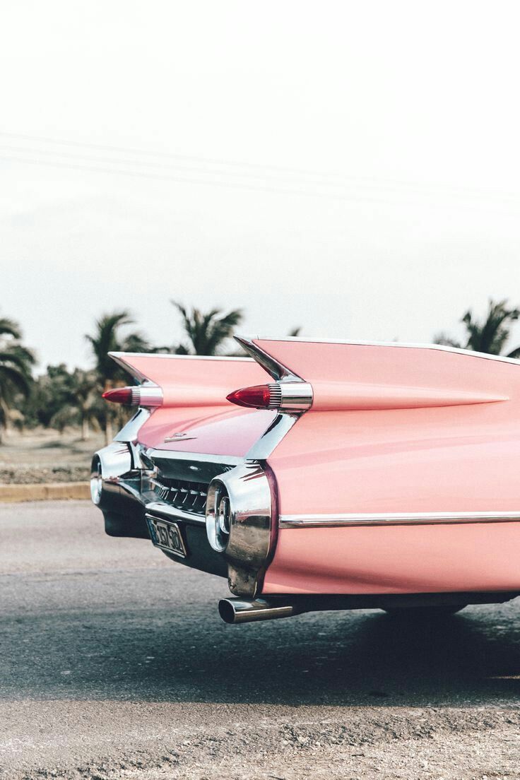 A pink car is parked on the side of an empty road - Cars