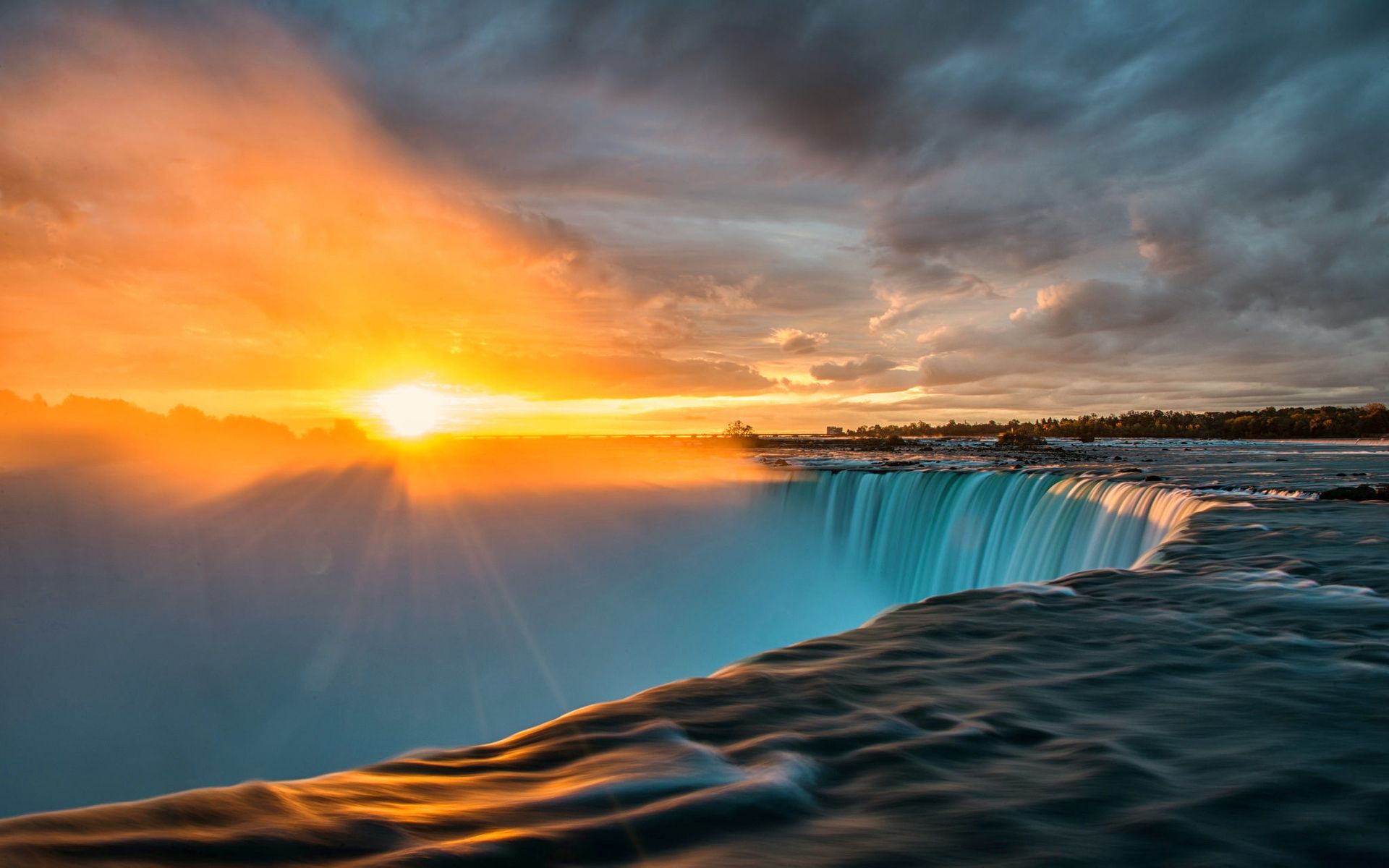 The sun rising over a waterfall with a dark sky above - Sunset