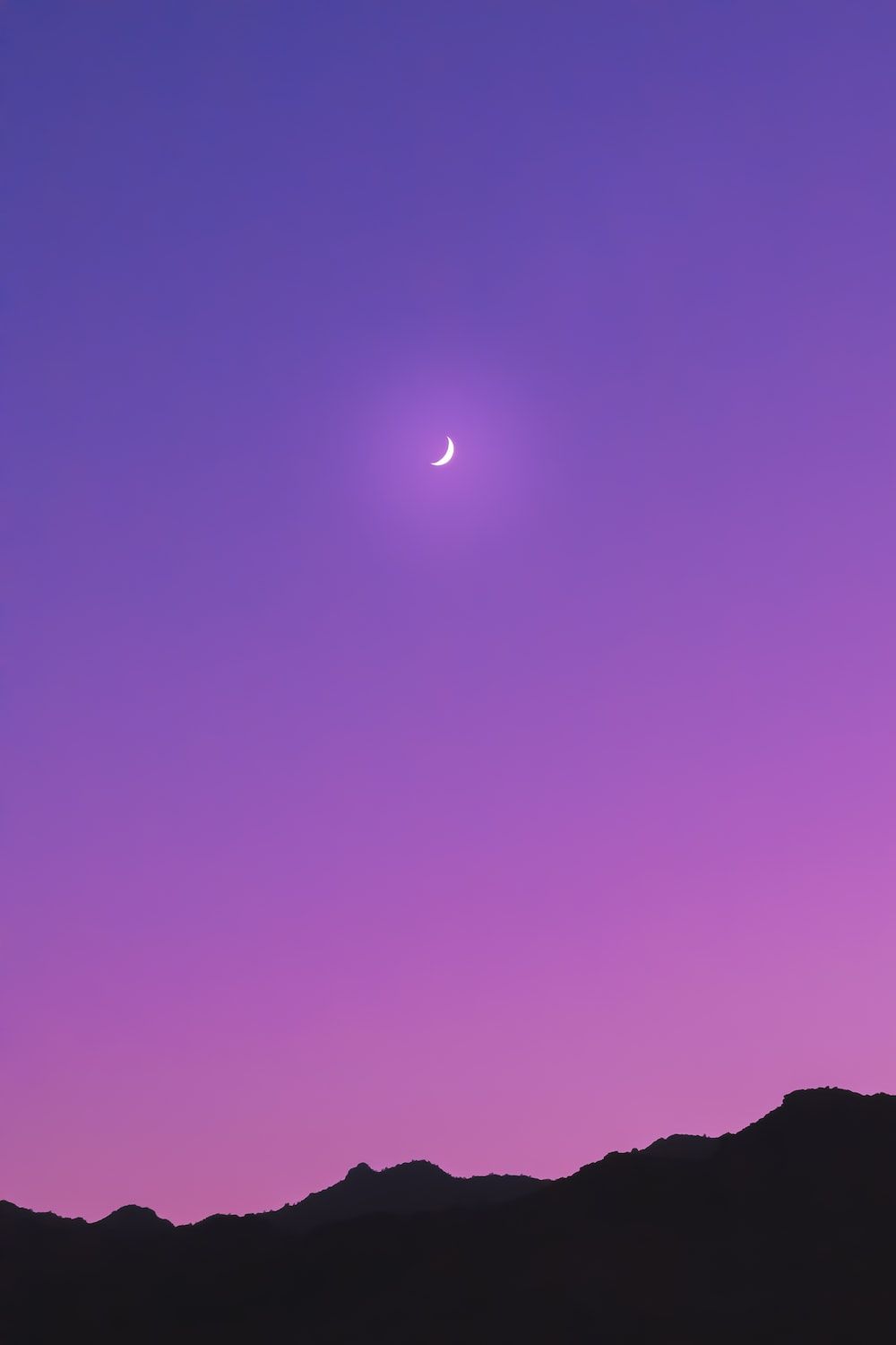 A crescent moon in a purple sky above a mountain range - Night