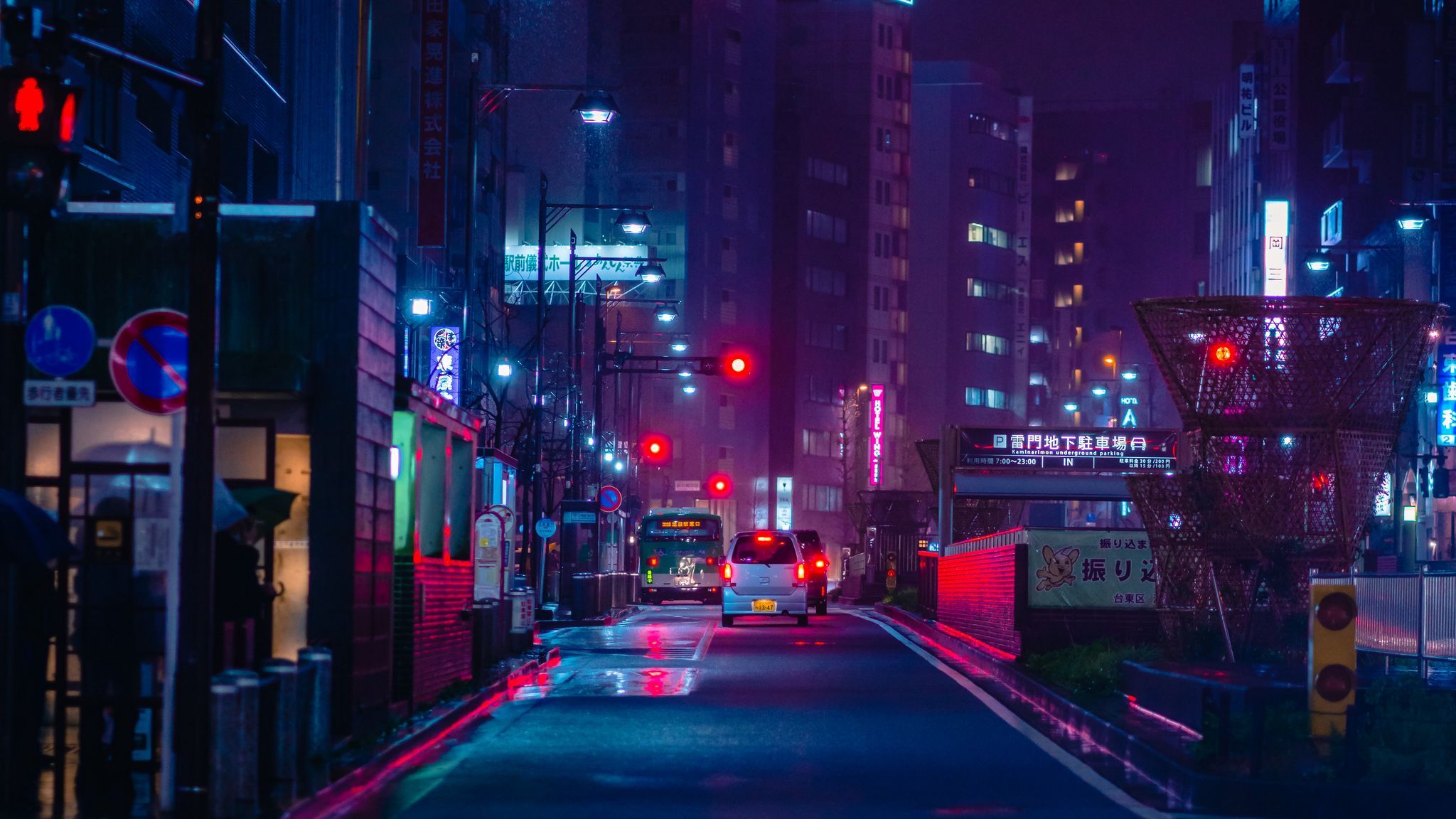 A Tokyo street at night with neon lights and a red traffic light. - Night