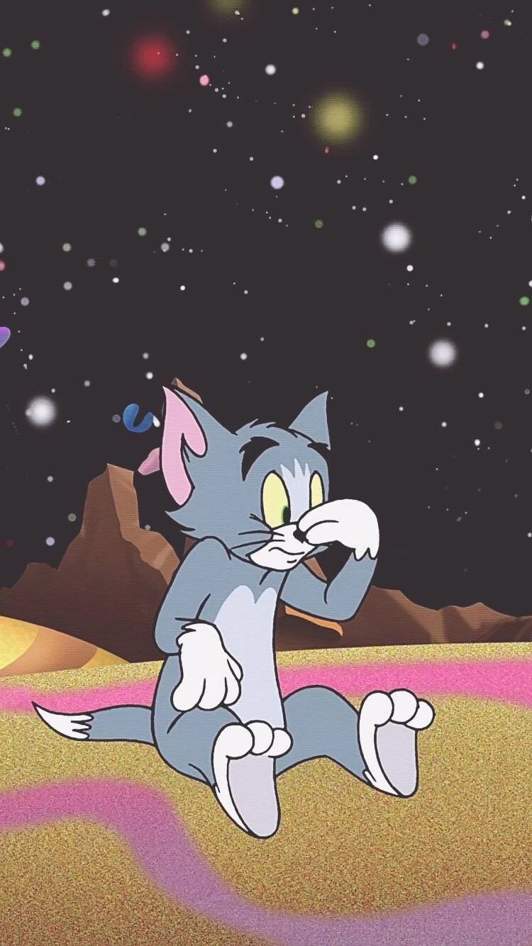 A cartoon image of a grey cat with pink ears and tail, sitting on a rug in front of a desert-like background with a black sky full of stars. - Tom and Jerry